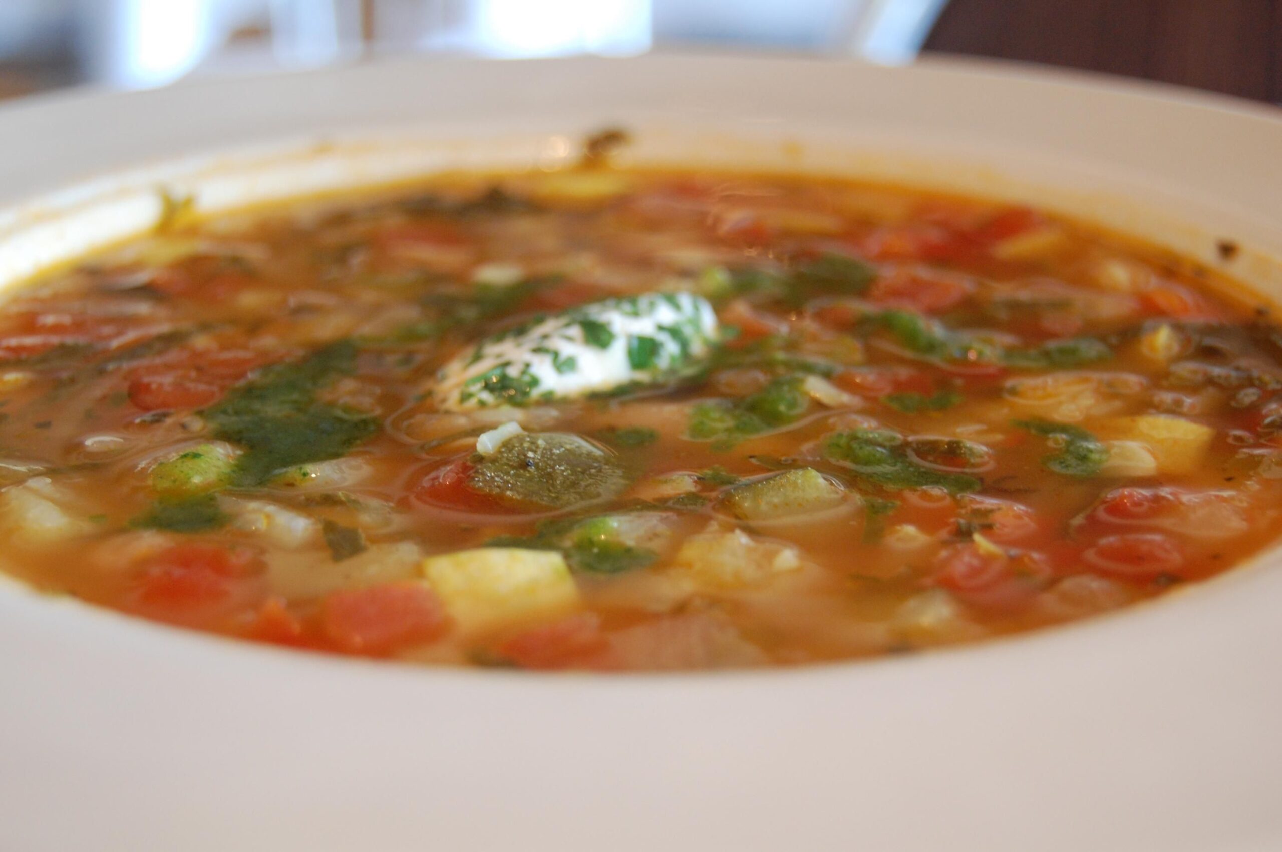 Close up of vegetable soup in a white shallow bowl with sour cream dollop and fresh herbs
