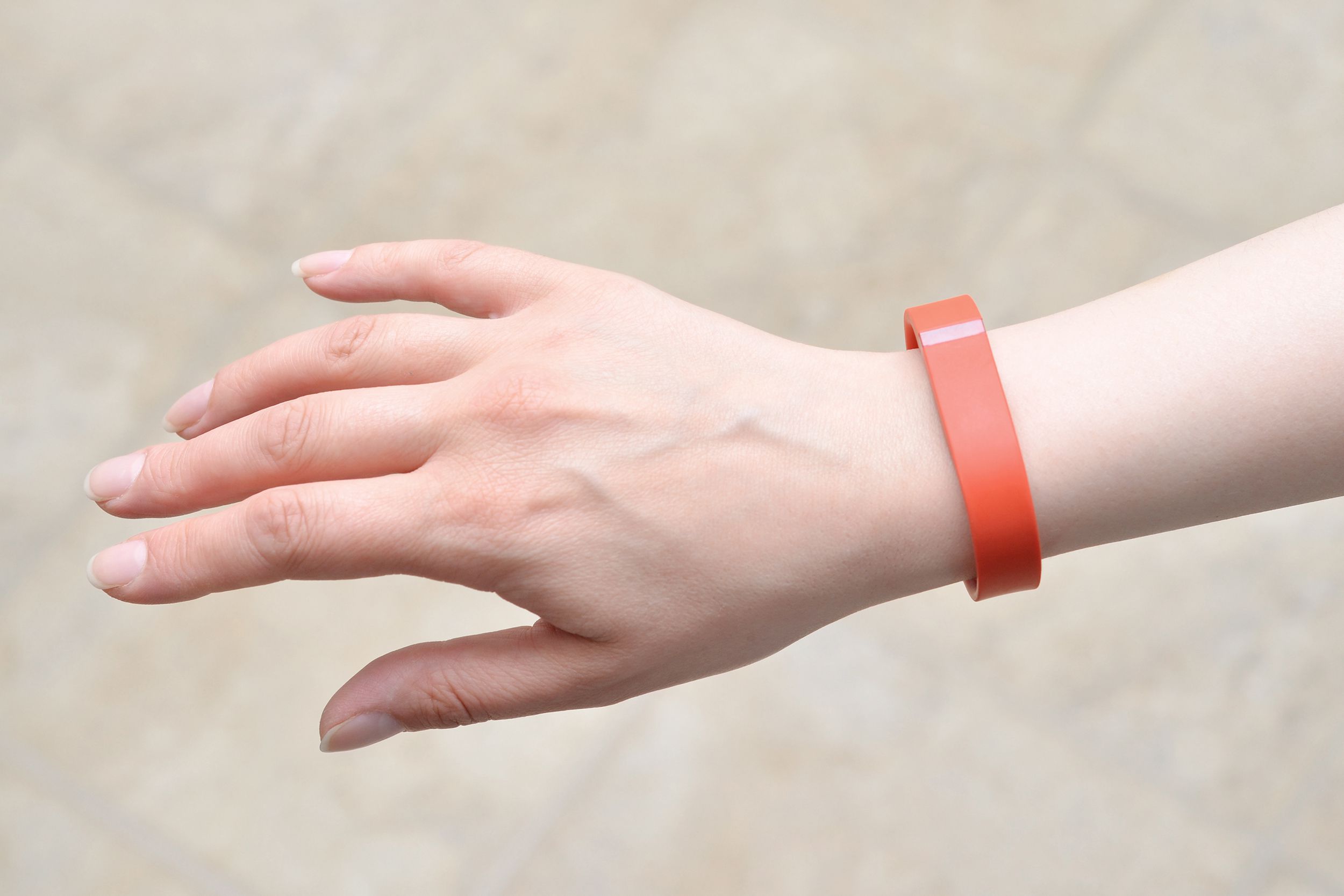 Woman wearing a red Fitbit Flex on her wrist, showing her hand and top of arm, against a blurred beige background