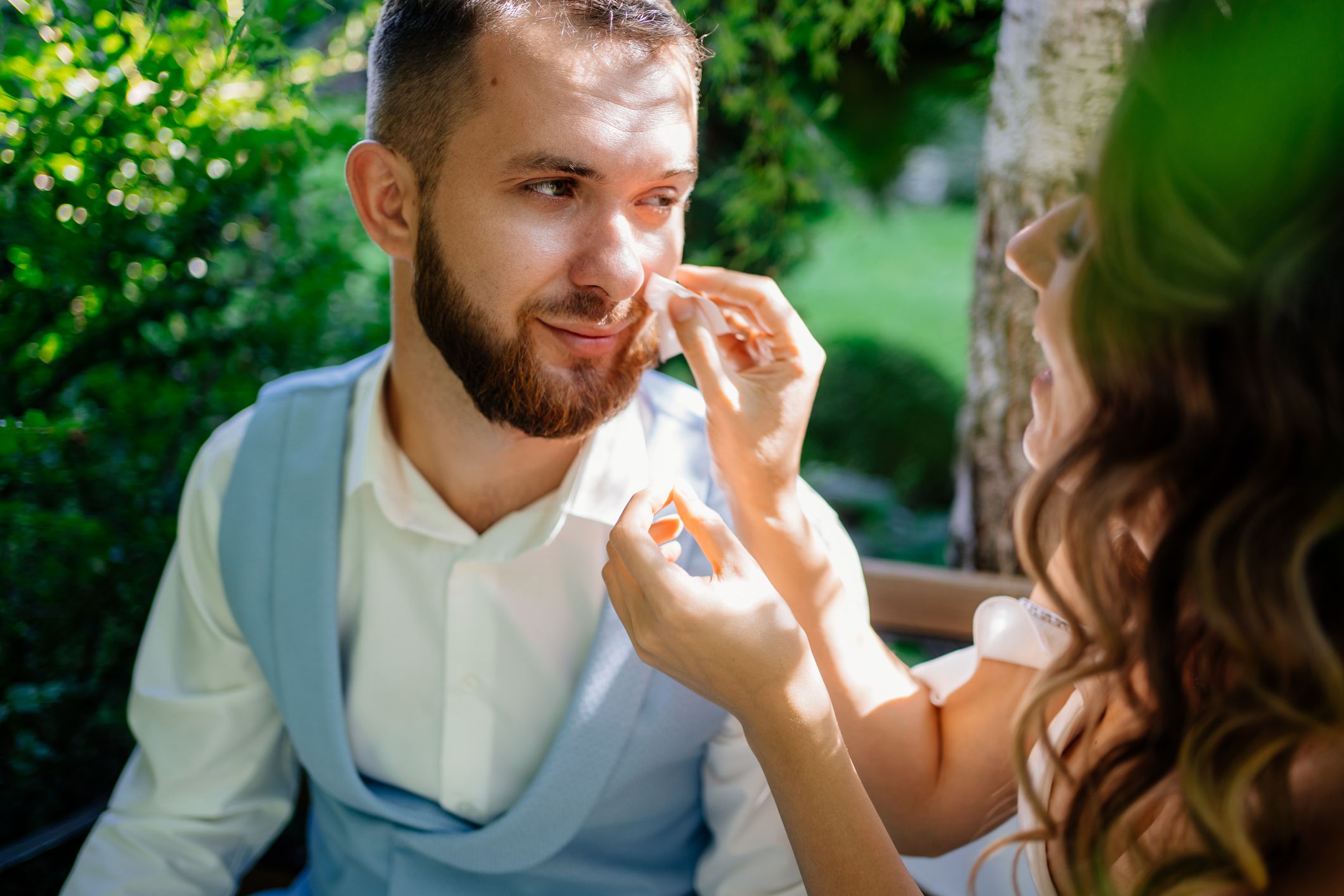 the bride gently and carefully wipes the face of the groom away sweat in the heat. Walk for a wedding photo shoot in the park.