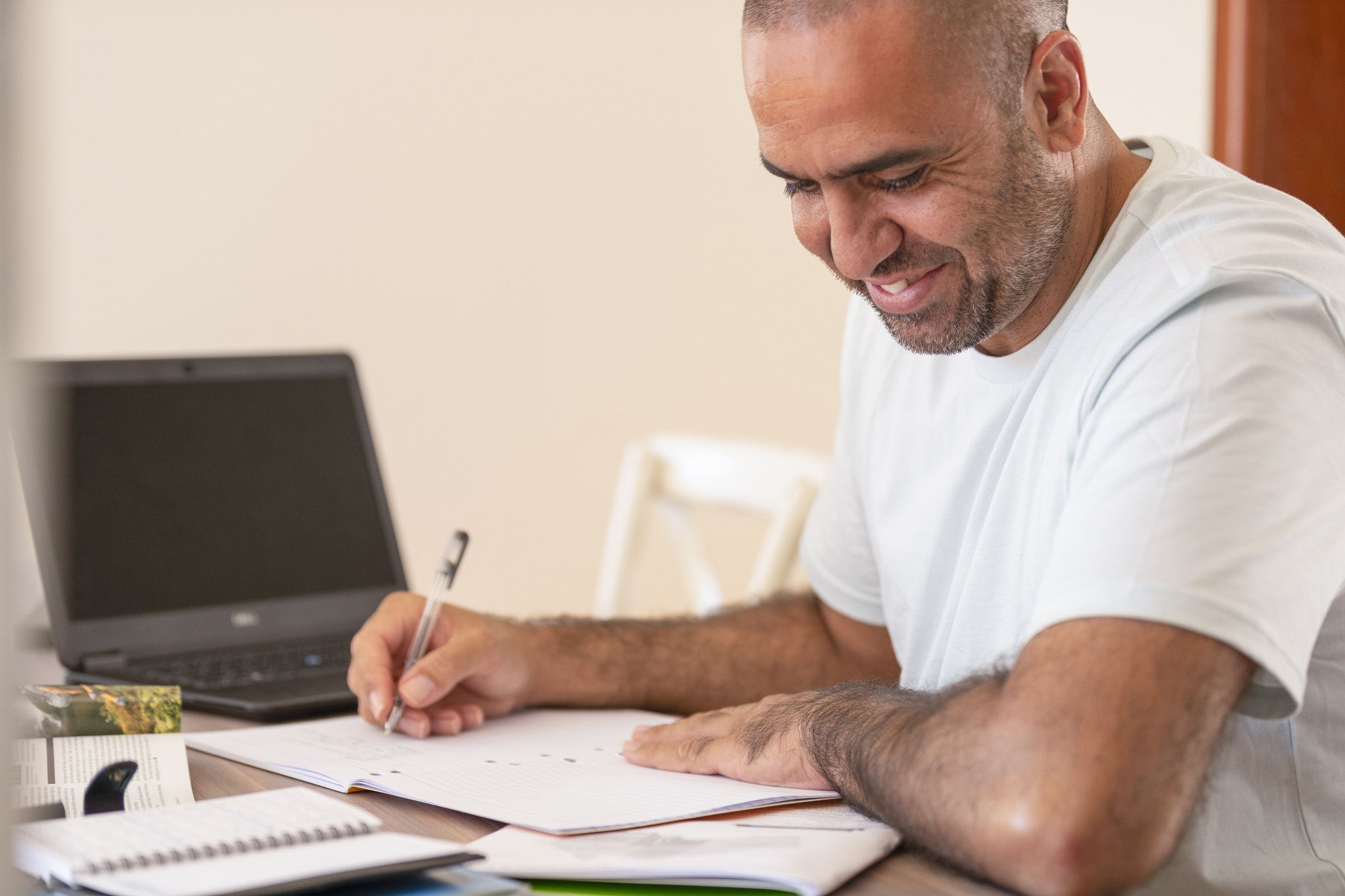man looking at different booklets taking notes, laptop in background