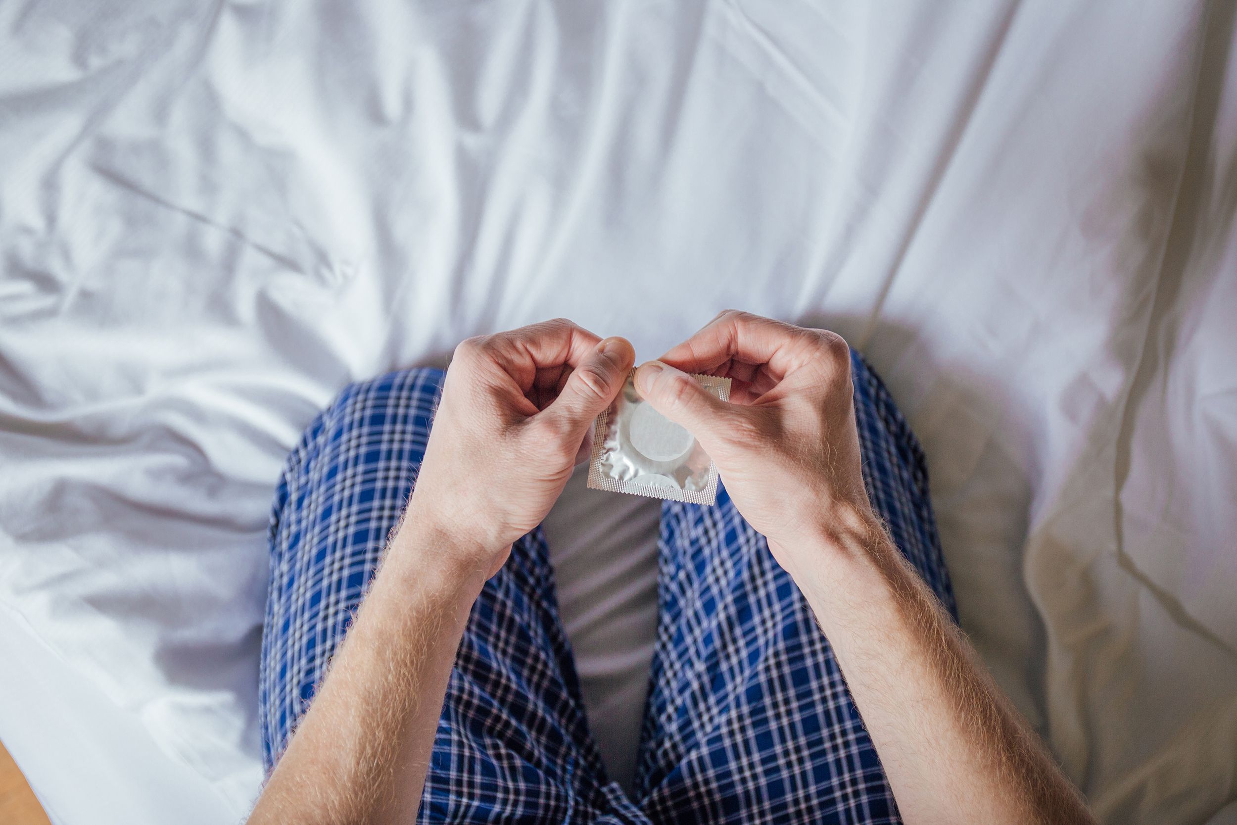 man opening condom while sitting on bed