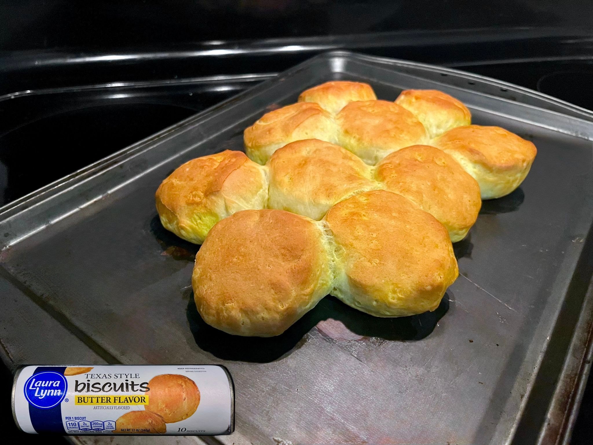 A baking sheet holds nine golden-brown biscuits grouped together, freshly baked. In the corner, a package labeled "Laura Lynn Texas Style Biscuits Butter Flavor" is shown for reference.