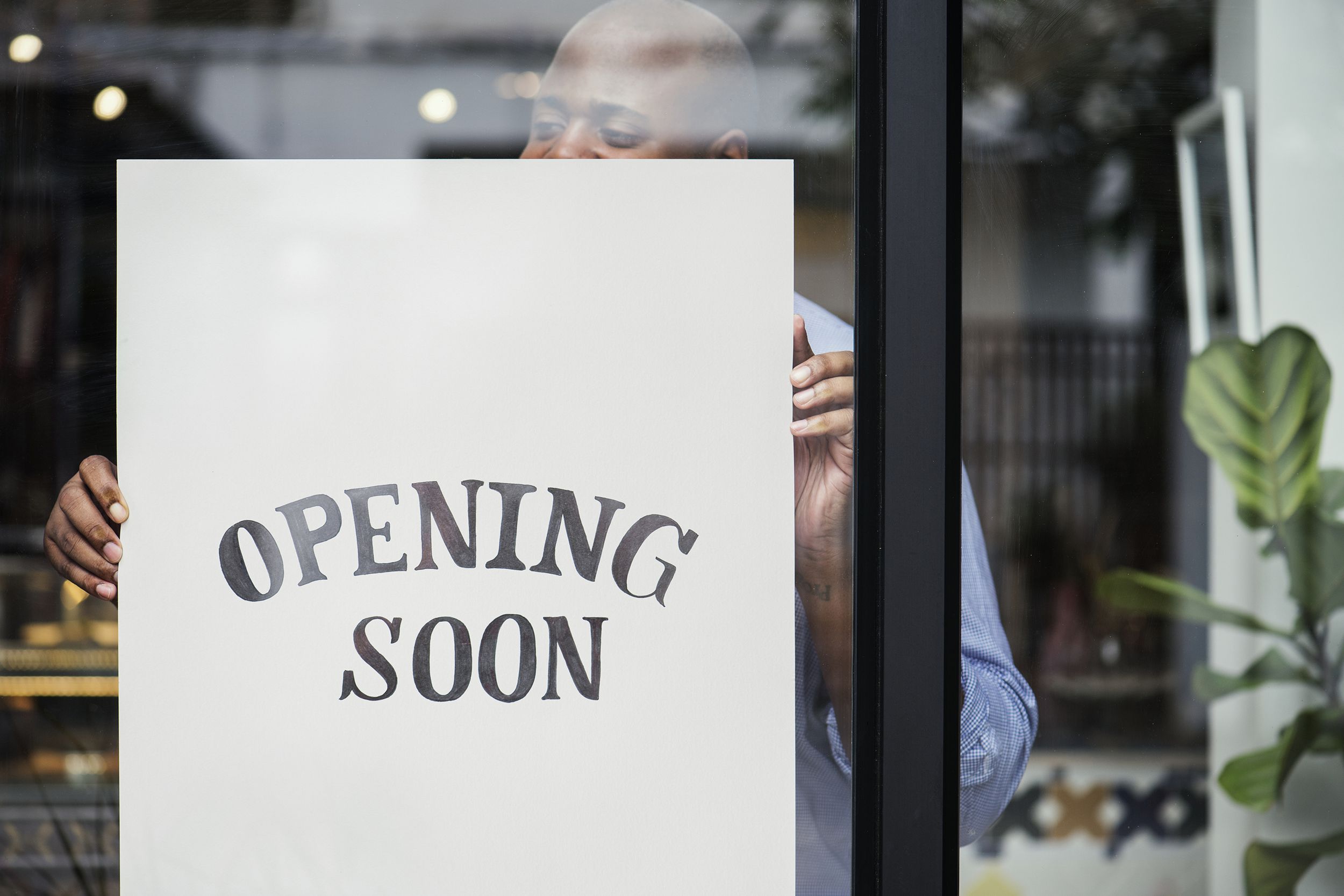 man putting on store opening soon sign