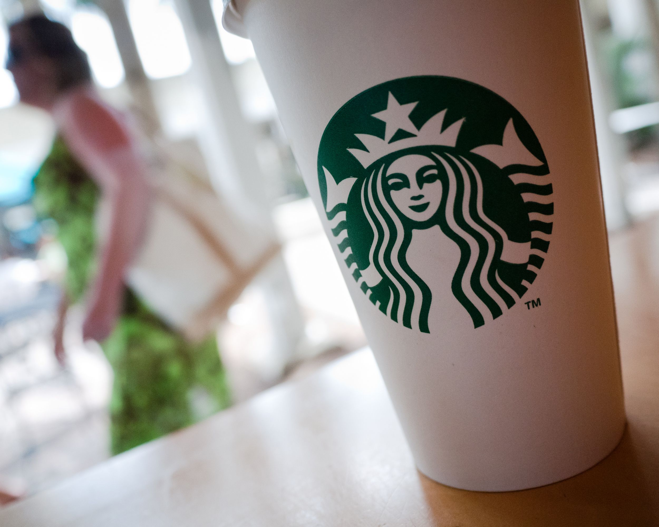 woman walks behind a Starbucks Coffee cup, outside of a Starbucks Coffee shop located in Naples, Florida