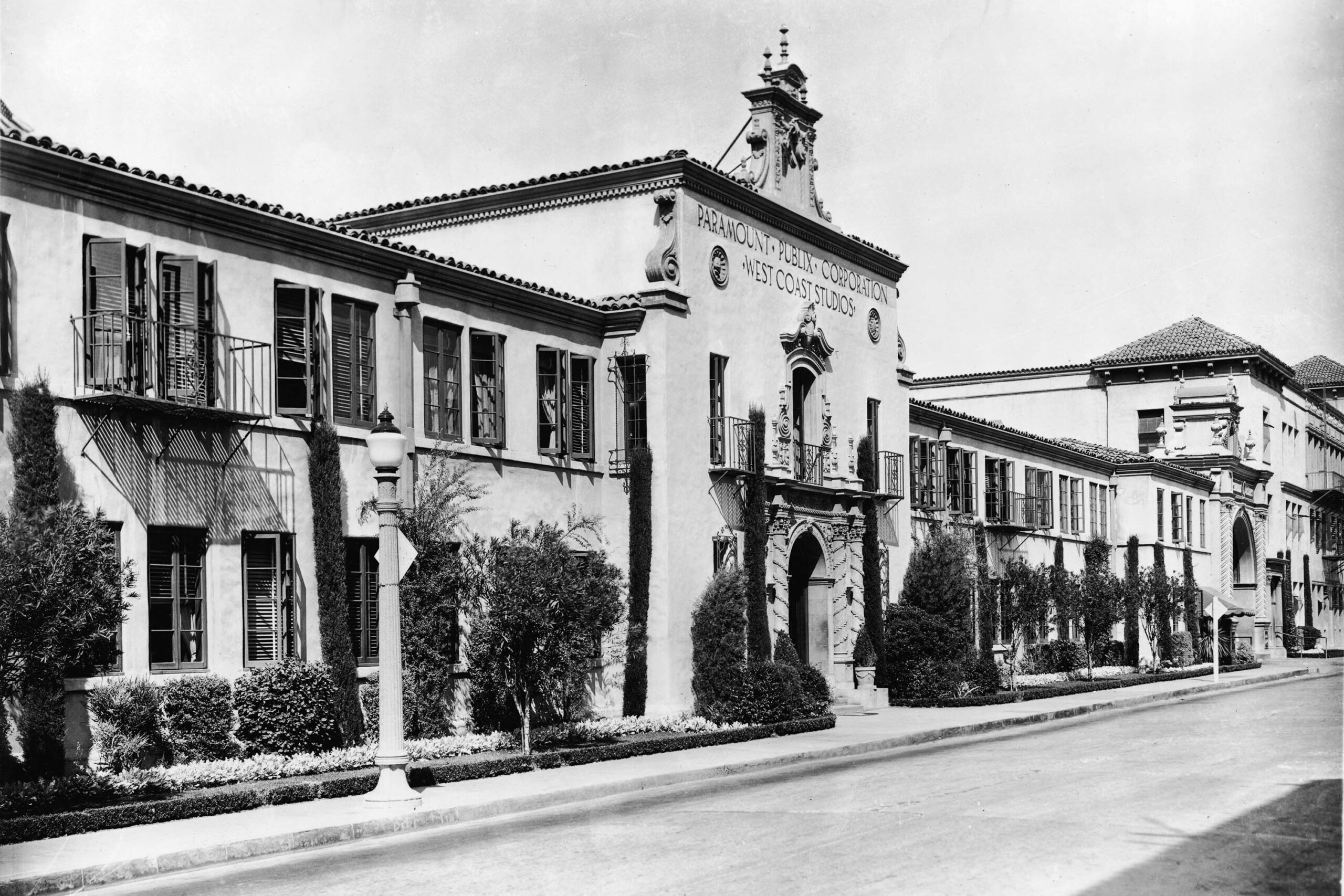 Historic black-and-white photo of the Paramount Pictures studio building in Hollywood, featuring Spanish Colonial Revival architecture, arched entrance, and decorative details along a quiet street.