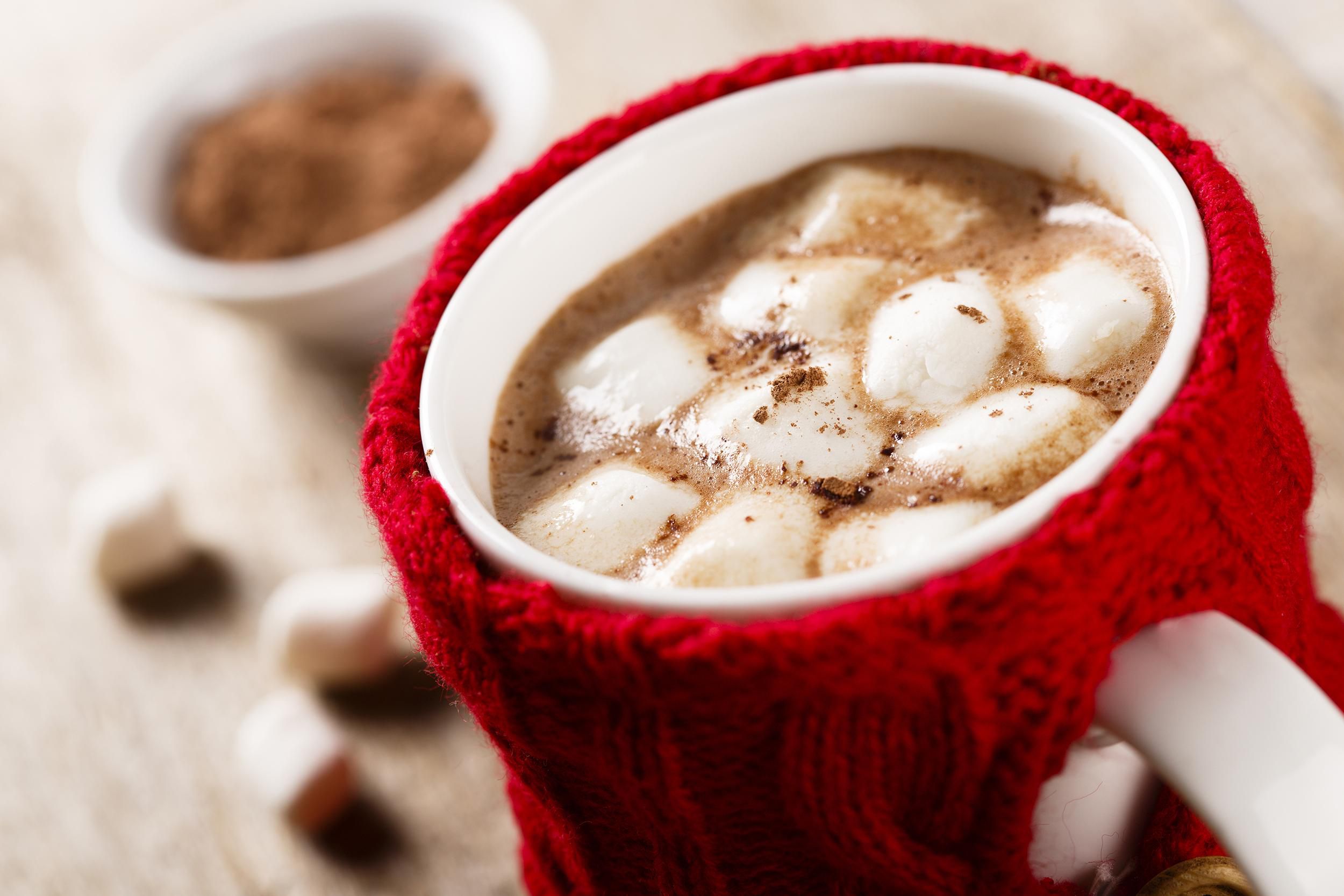 Hot cocoa drink with marshmallows in a white mug with a red woven cozy