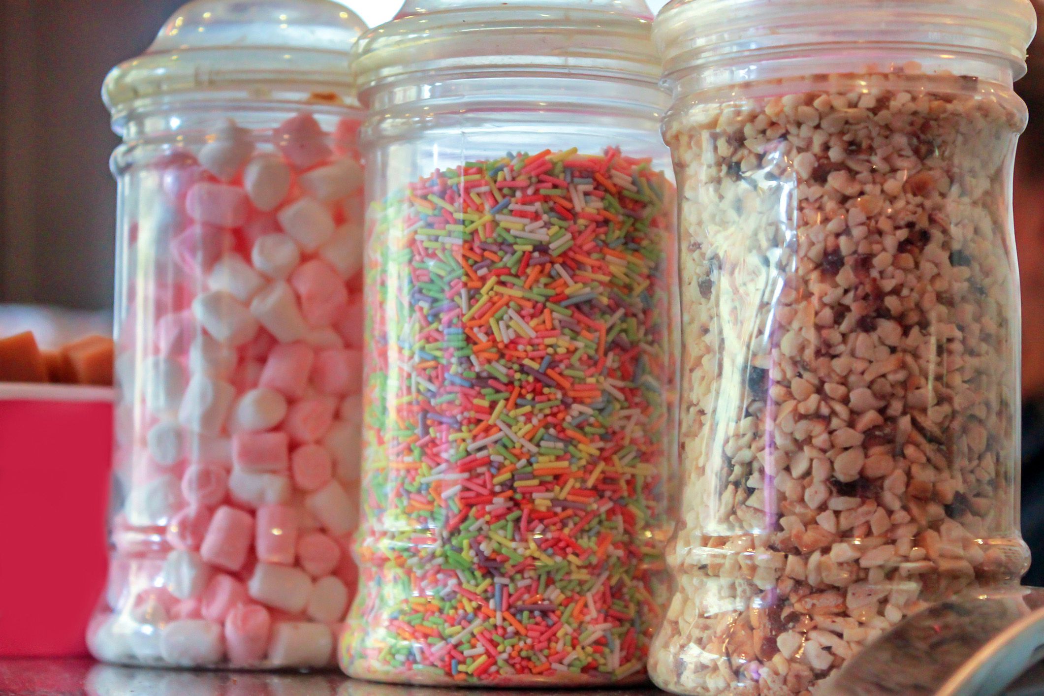 Ice cream toppings in glass jars, including tiny pink and white marshmallows, sprinkles and crushed nuts