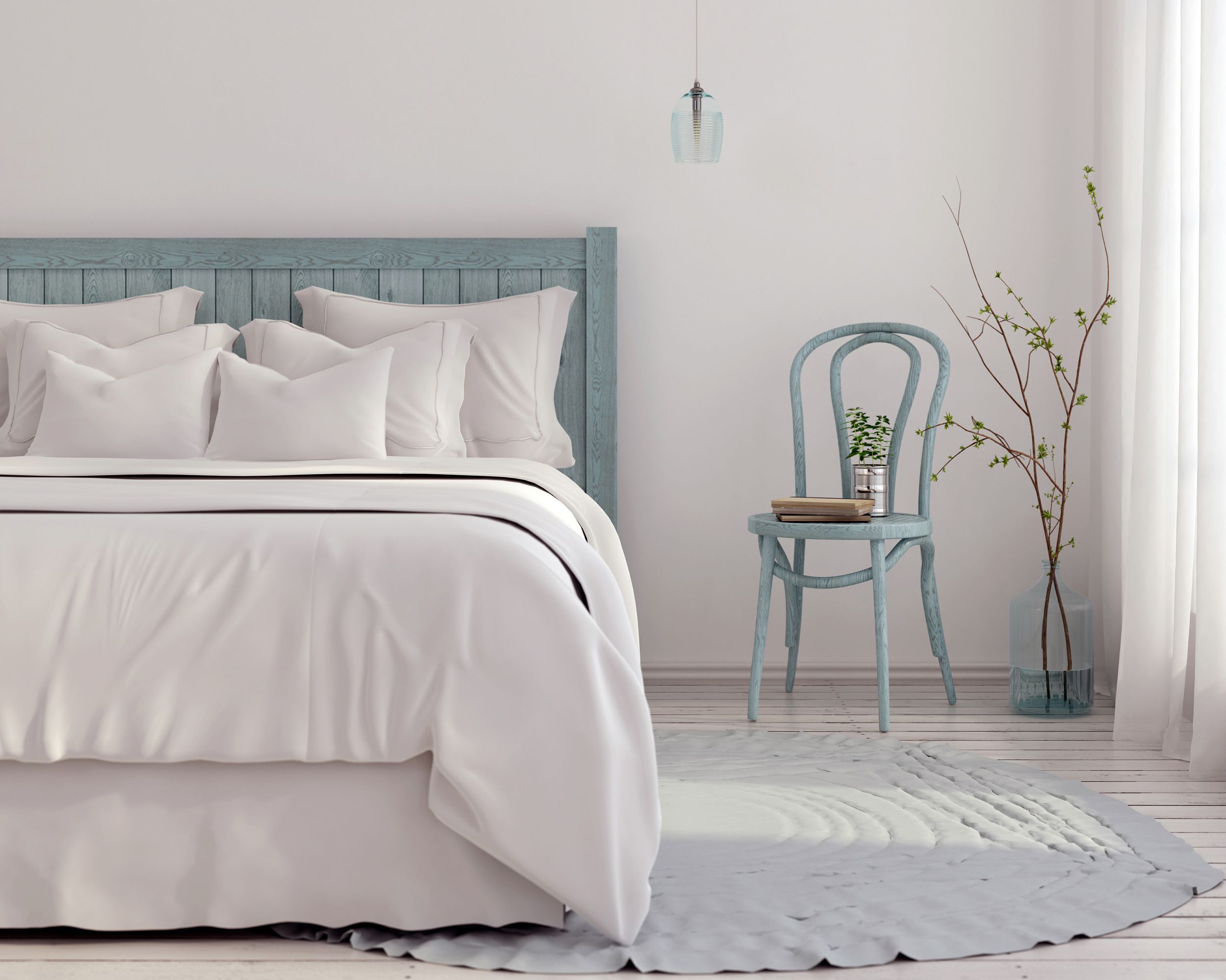Soothing bedroom with bedding, a small chair, a light hanging from ceiling, a rug, and a plant with a window on the right, colors are white and grey-blues