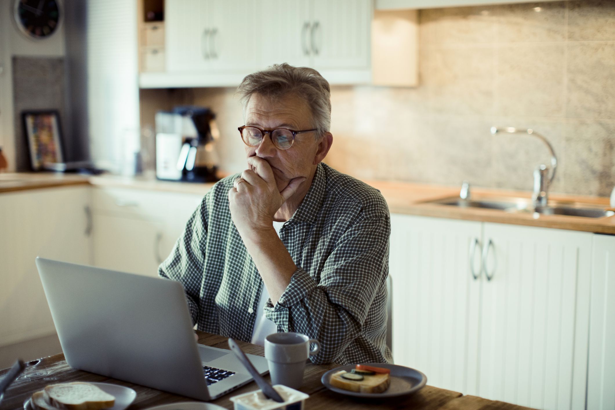 Man sitting in kitchen while on computer.