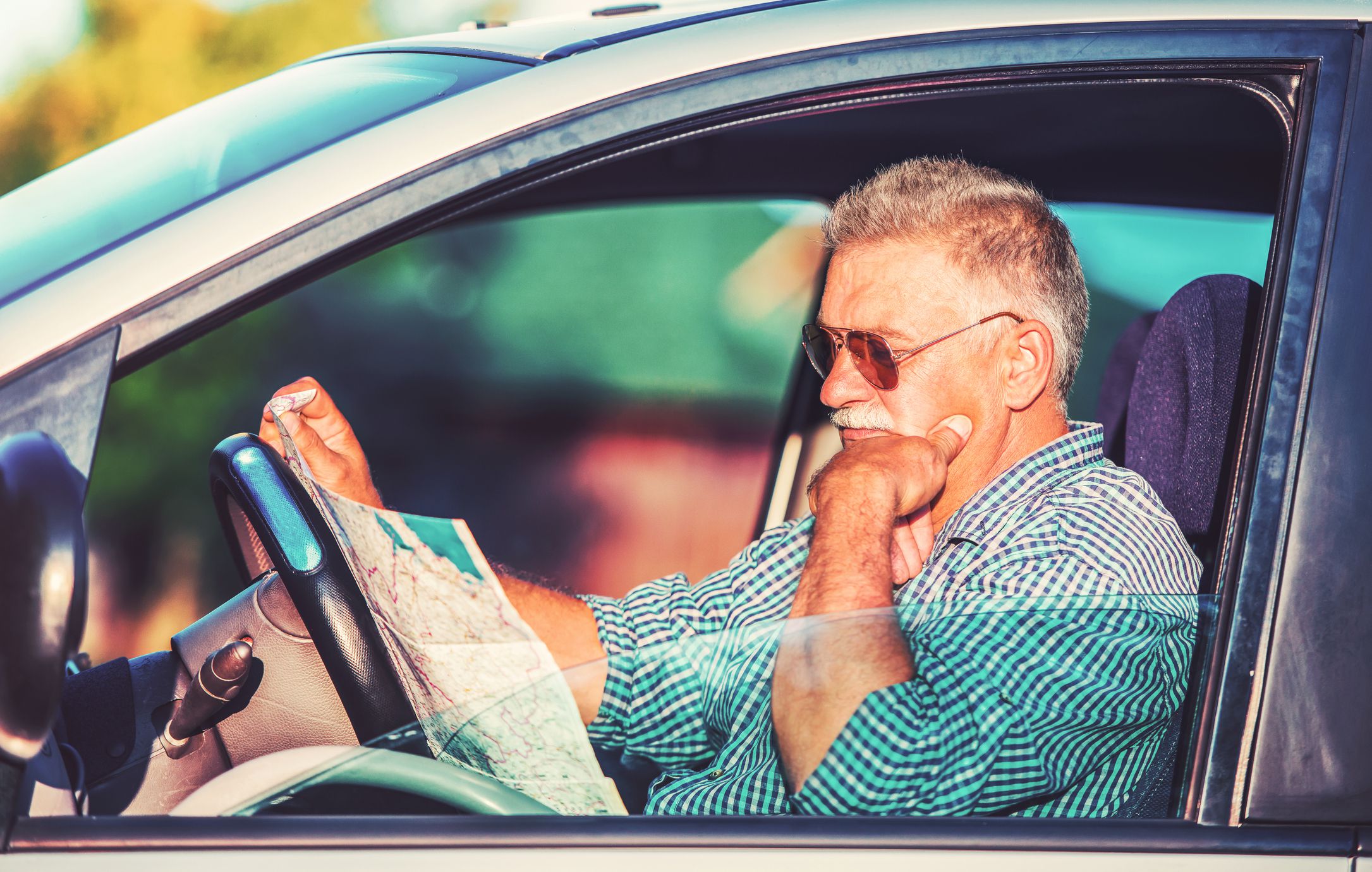 Bad navigation. Senior man having a problem with orientation on the road during his journey with a car. He looking at map and try to find the missed road. Traveling and transportation concept