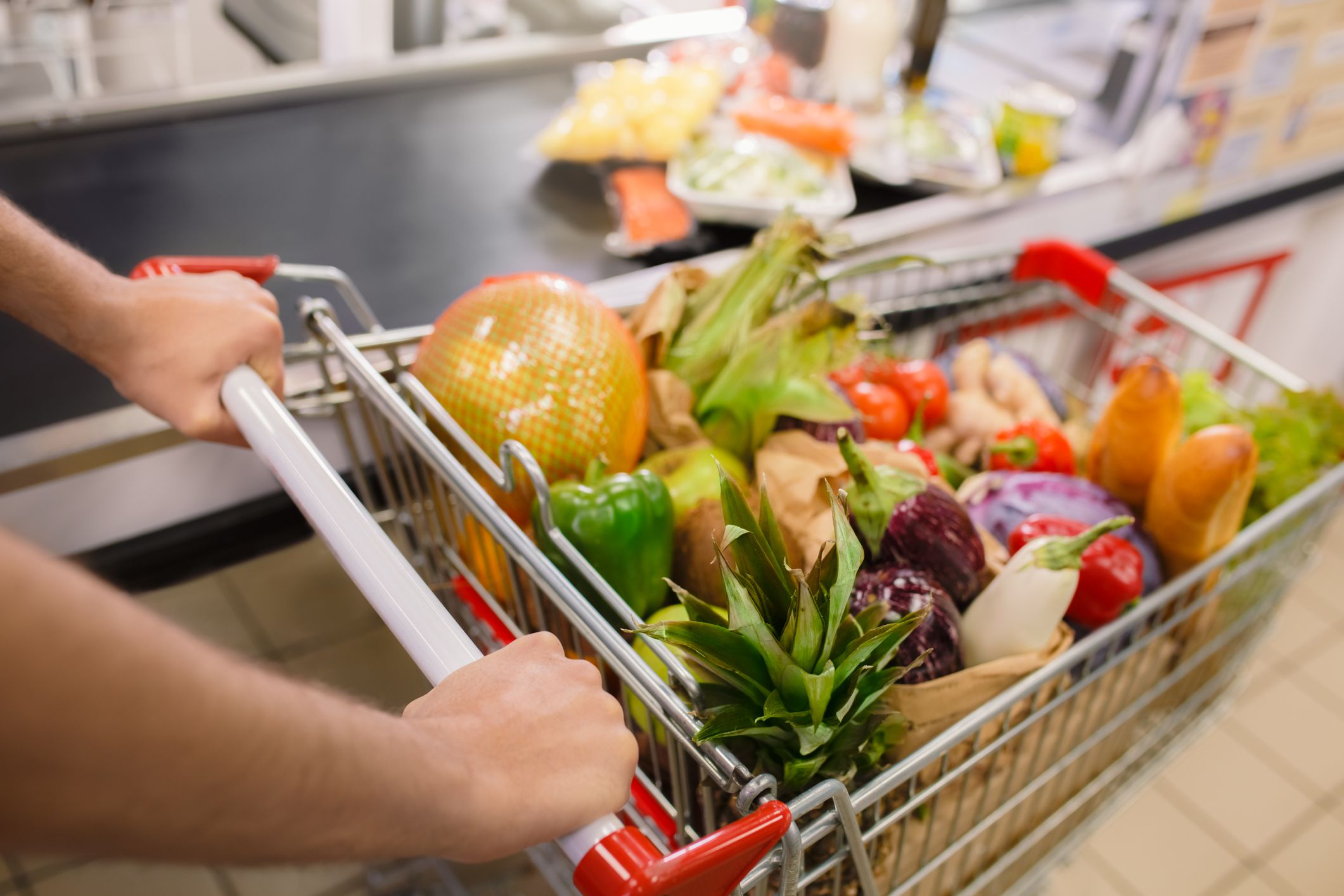 A customer with a shopping cart while checking out at a food store.