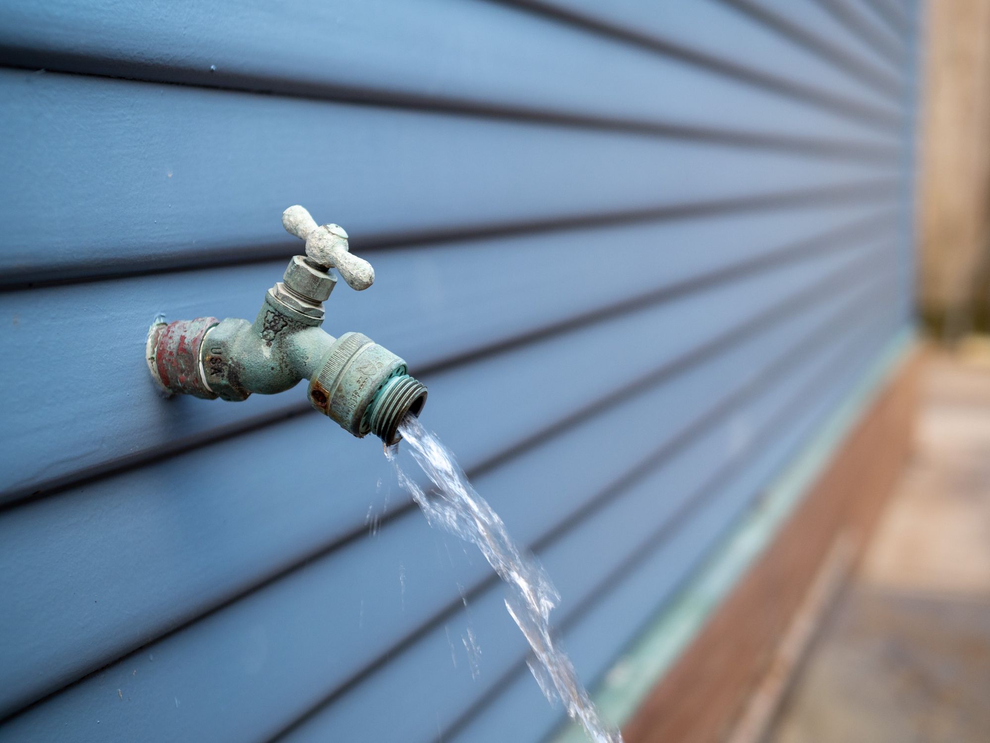 Water streaming out of outdoor faucet for garden hose outside home