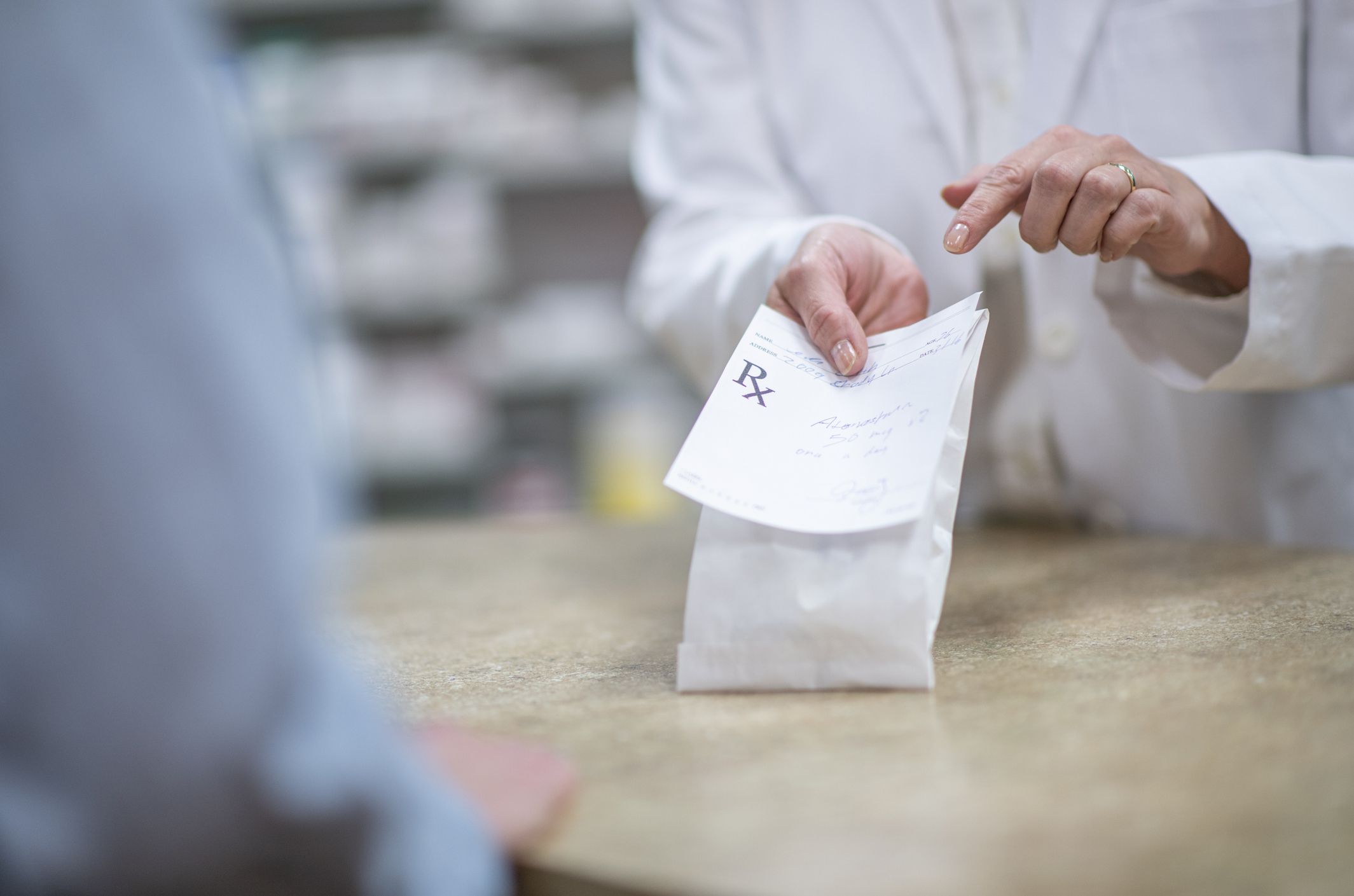 A pharmacist handing a customer a packaged prescription.