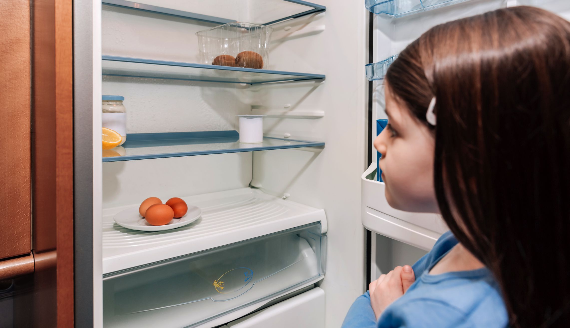 Worried girl looking at the almost empty fridge due to a crisis