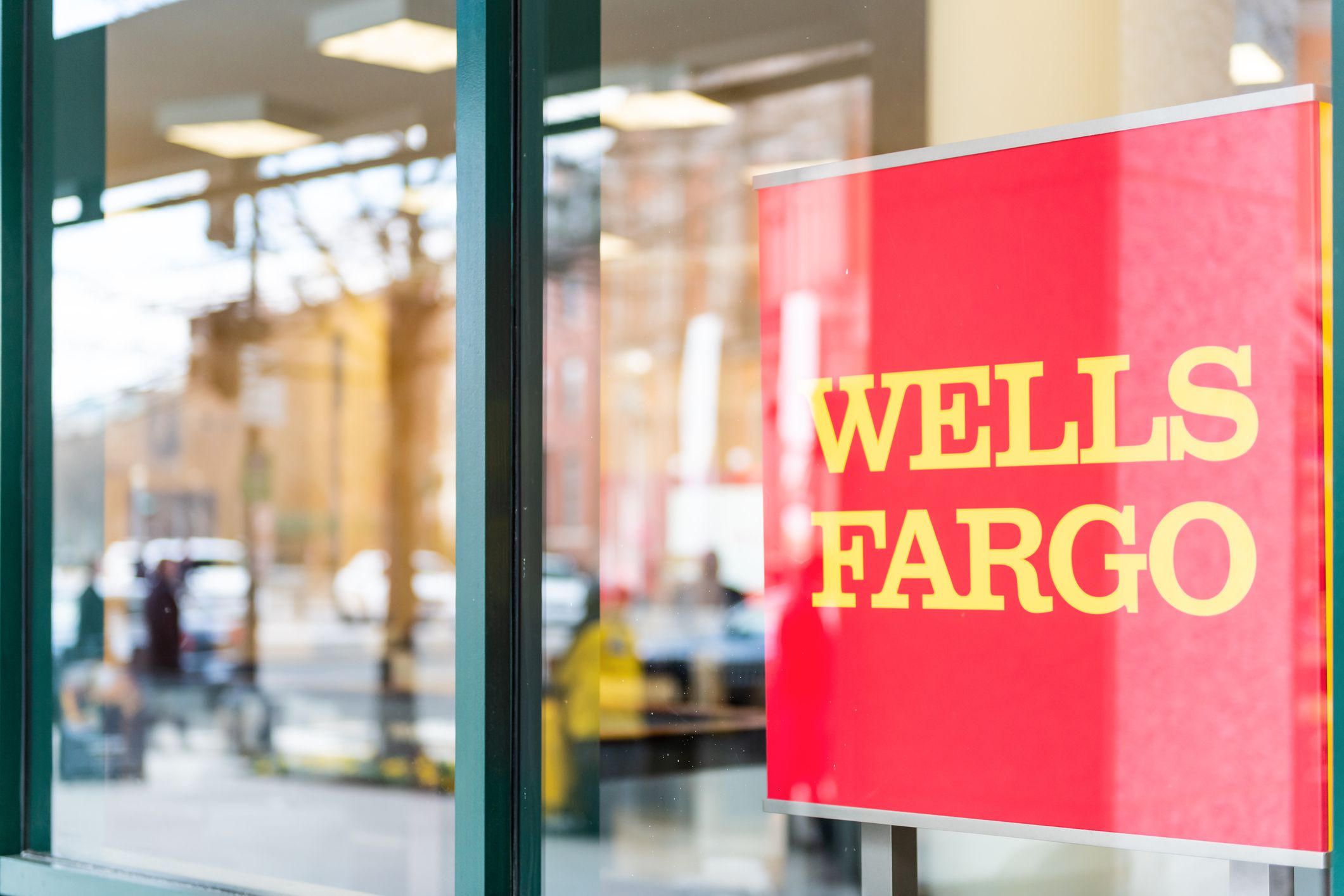 Washington DC, USA - March 9, 2018: Closeup of Wells Fargo bank branch entrance with red, yellow sign, window reflection of people walking on sidewalk street