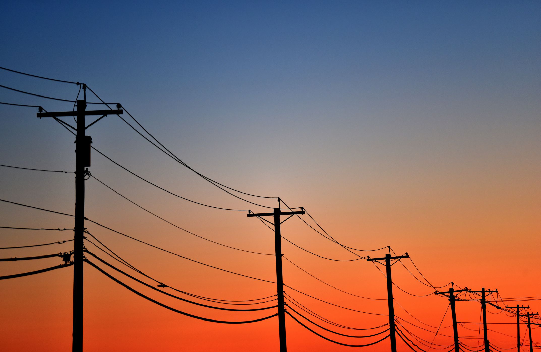 A line of telephone poles in front of a colorful sky at sunset.