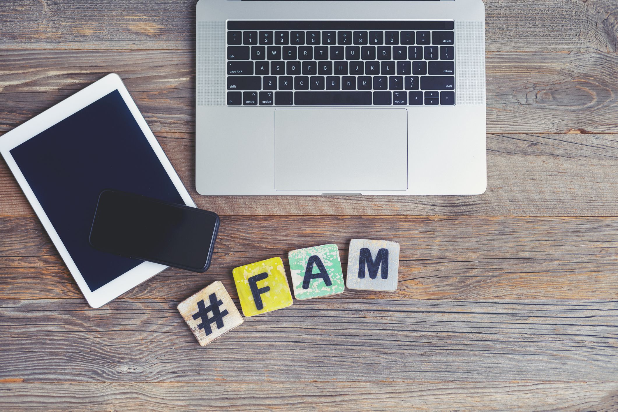 FAM, slang for family. Laptop, digital tablet and mobile phone with a hashtag and the letters FAM beside them. They are on a wooden background with copy space.