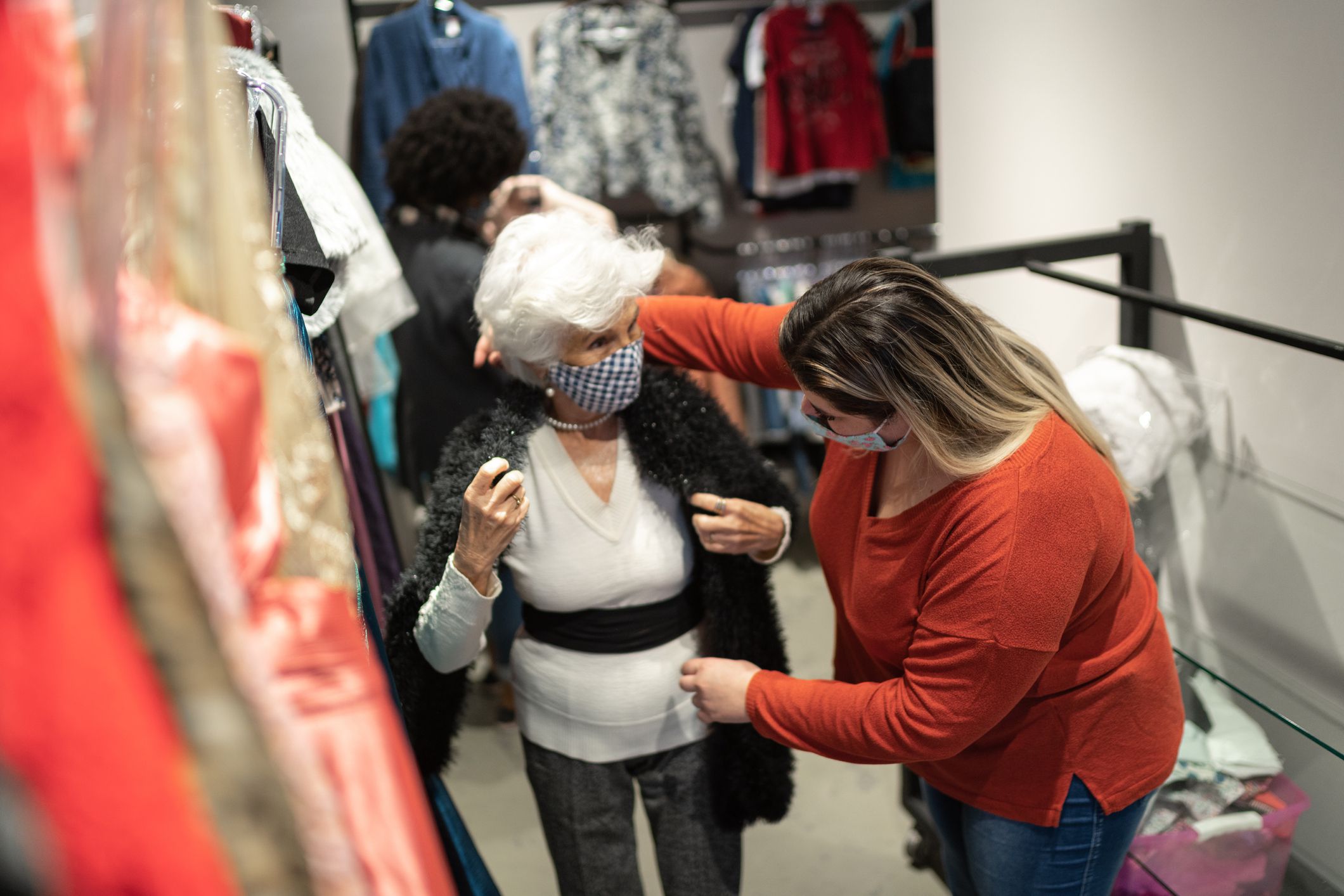 Senior woman wearing face mask being helped by a saleswoman while shopping for clothes in a thrift store