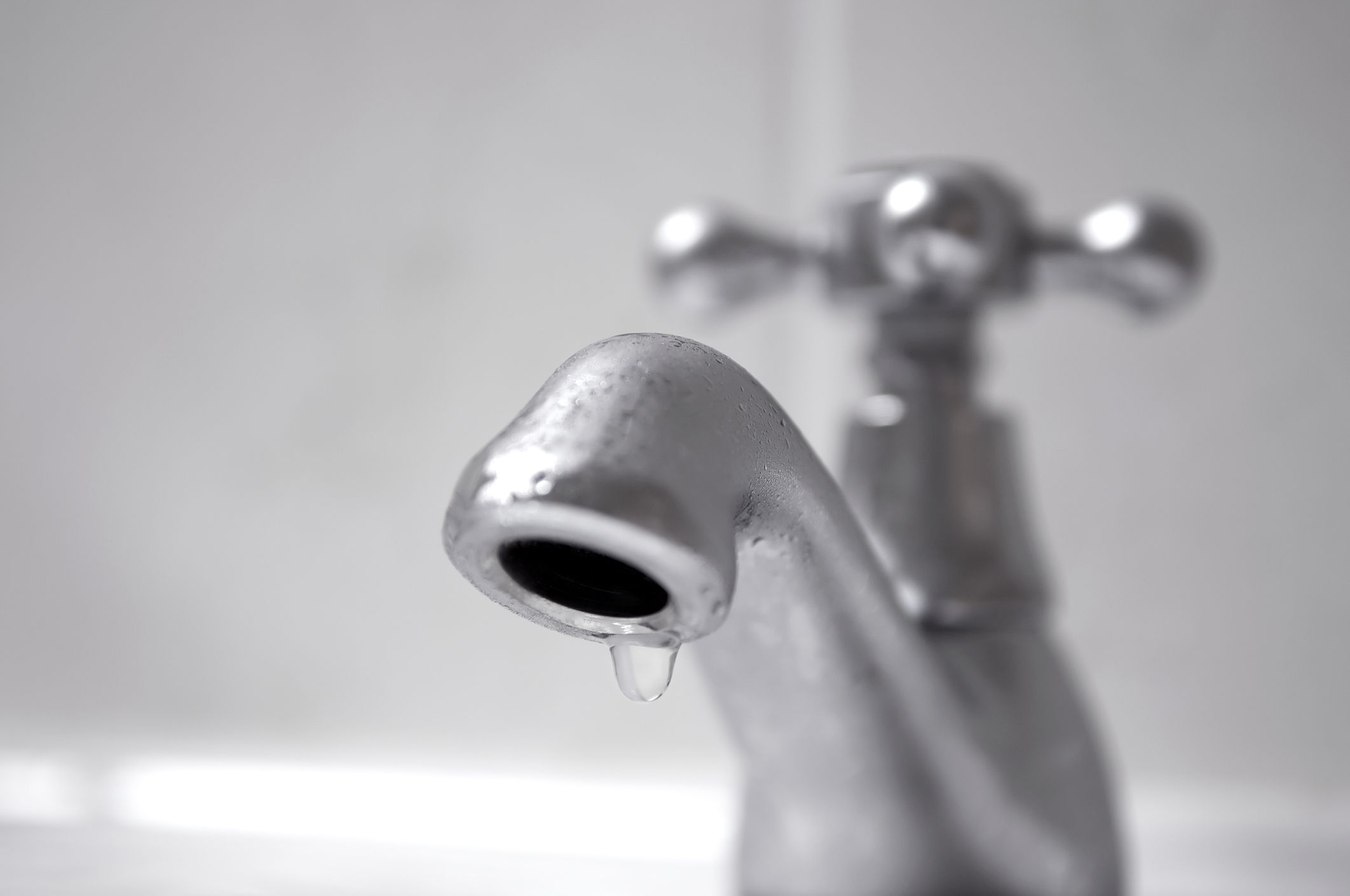 Close up of water drop on domestic chrome tap, shallow depth of field, water conservation concept.
