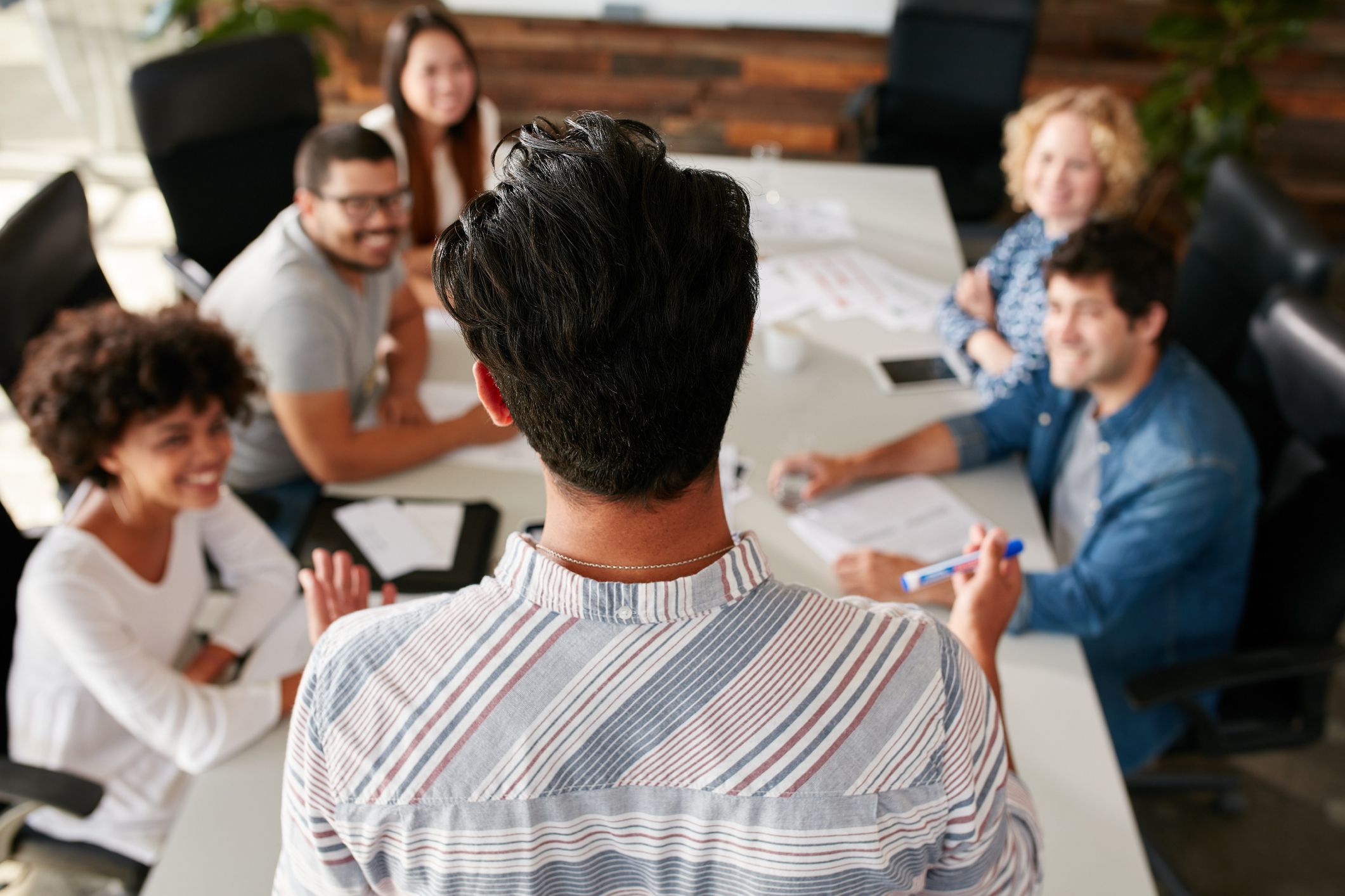 Rear view portrait of man explaining business ideas to colleagues during a meeting in conference room. Young people meeting in boardroom.