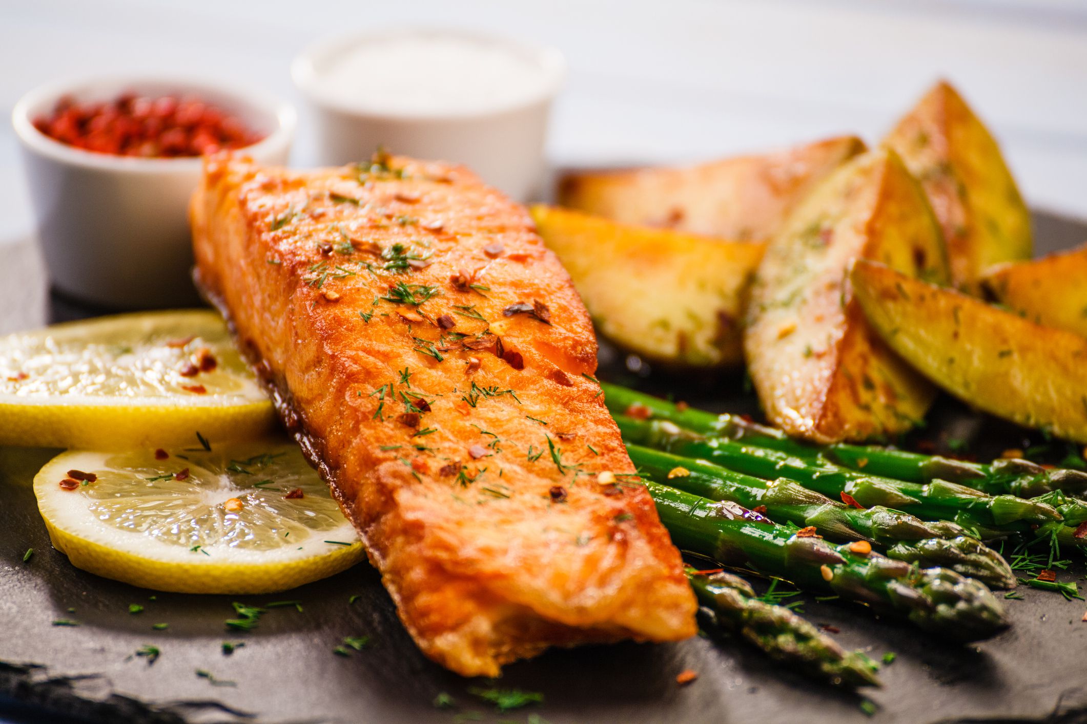 Grilled salmon with fried potatoes and vegetables served on black stone plate on wooden table