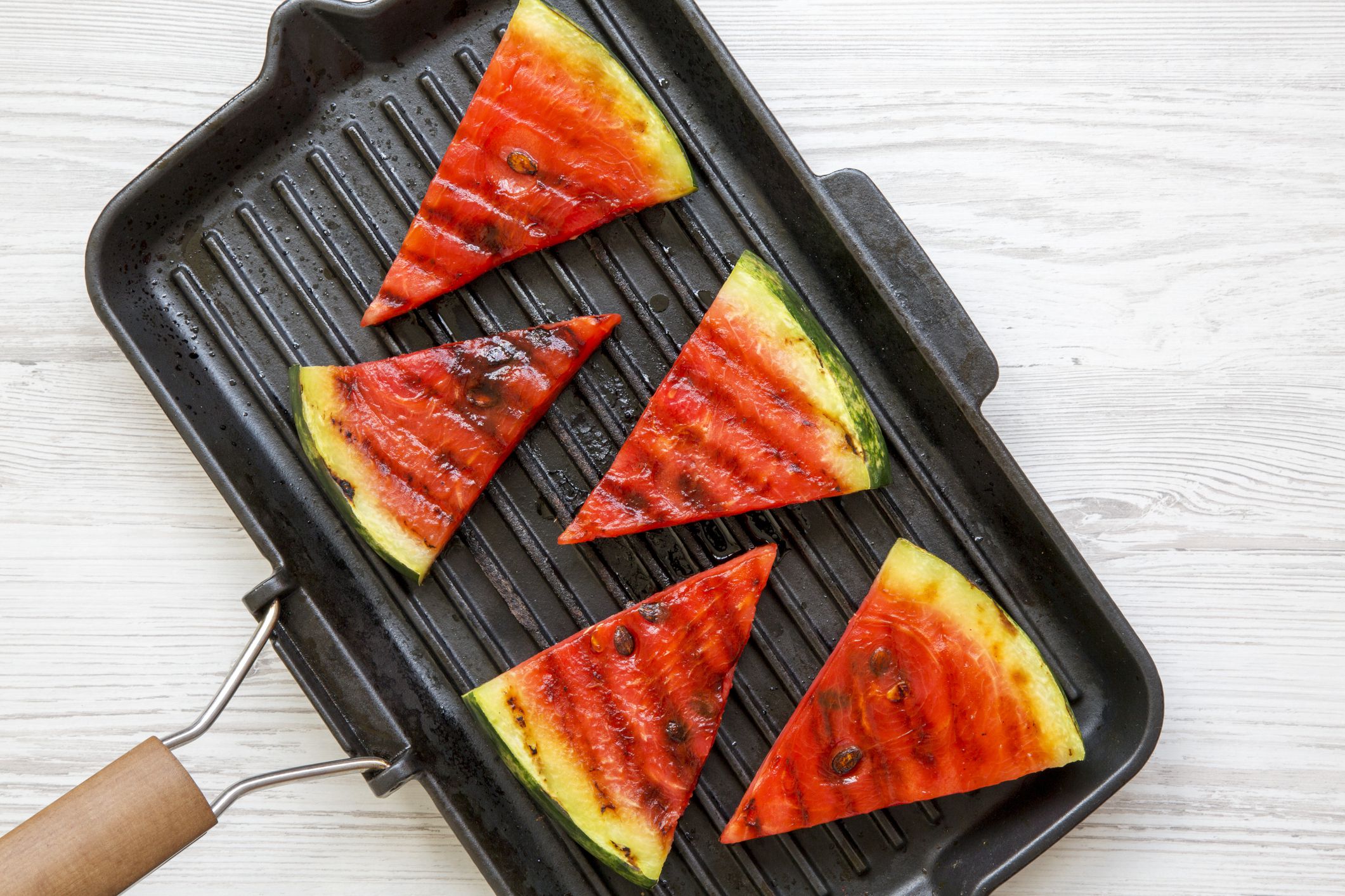 Slices of grilled watermelon in grilling pan on a white wooden table, top view. Healthy summer fruit. Closeup.