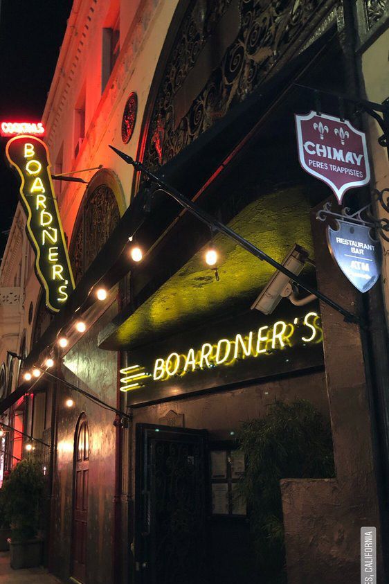 Nighttime street view of Boardner's bar entrance, with a glowing yellow neon sign, round lights above, and a red Chimay beer sign on the building's decorative exterior.