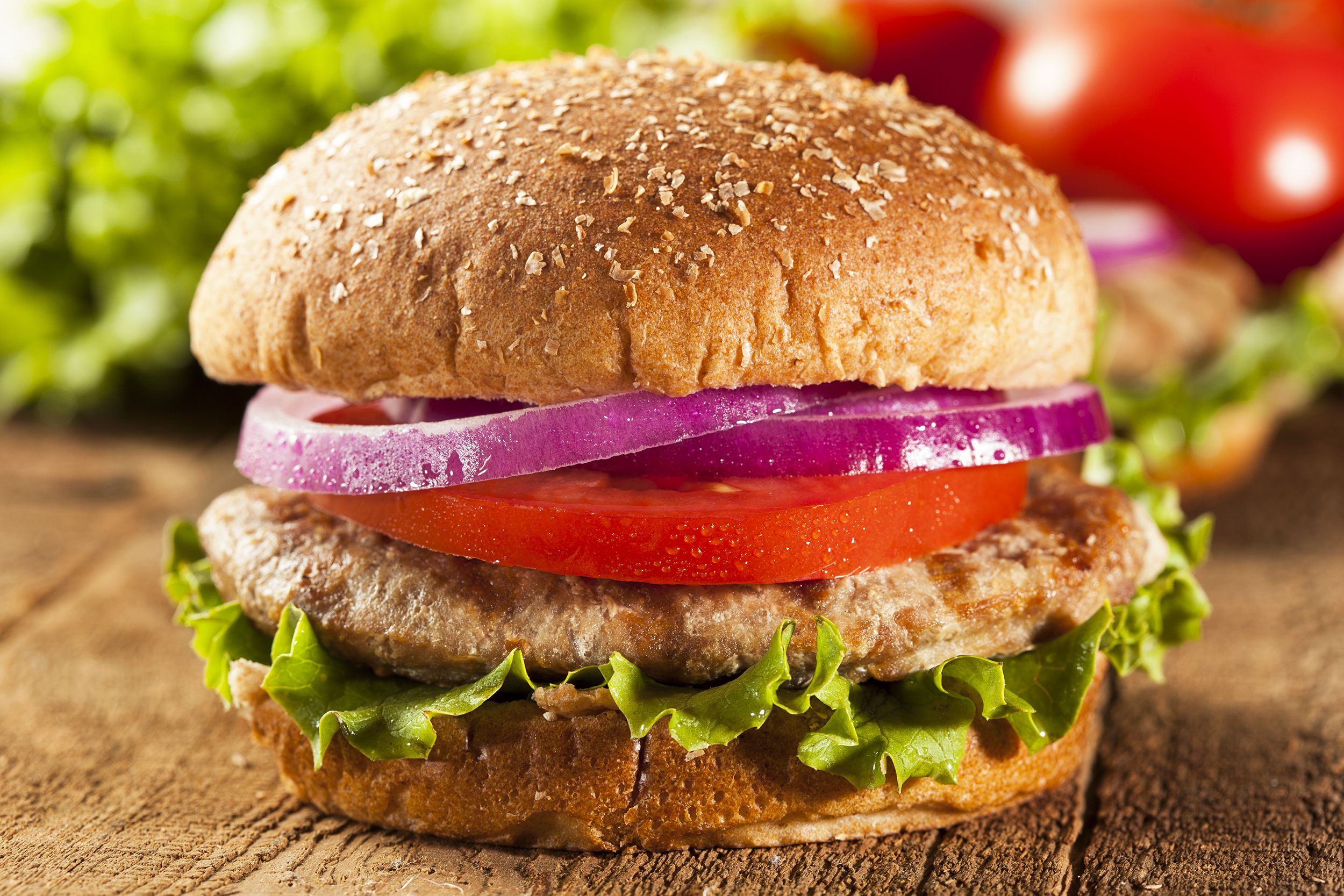 A best turkey burger with slices of onion, tomato, and lettuce, selective focus, on a rustic wooden table, with lettuce, tomatoes, and ingredients blurred in the background