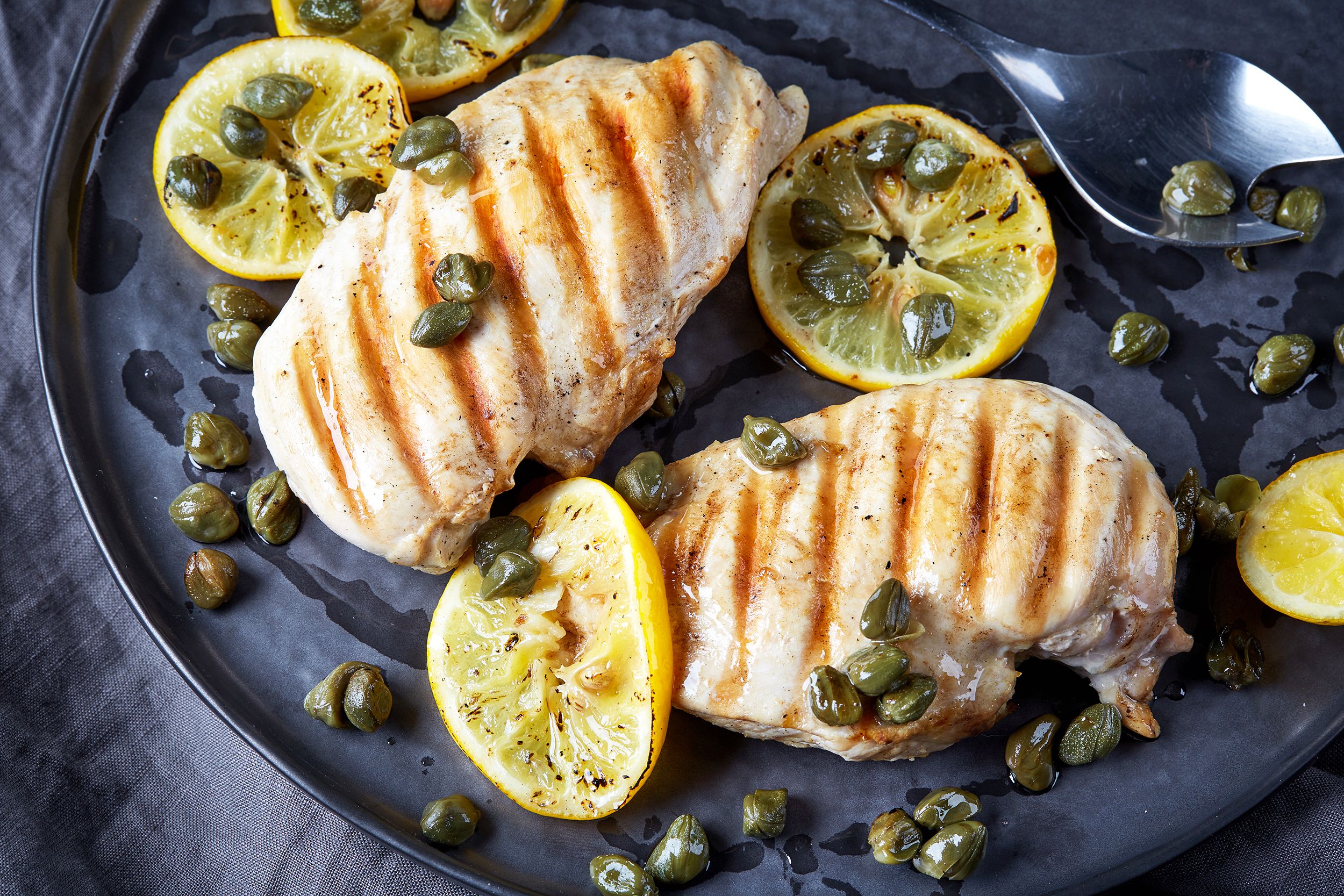 Chicken with lemon-caper sauce on a blue ceramic plate with a serving spoon on the top right