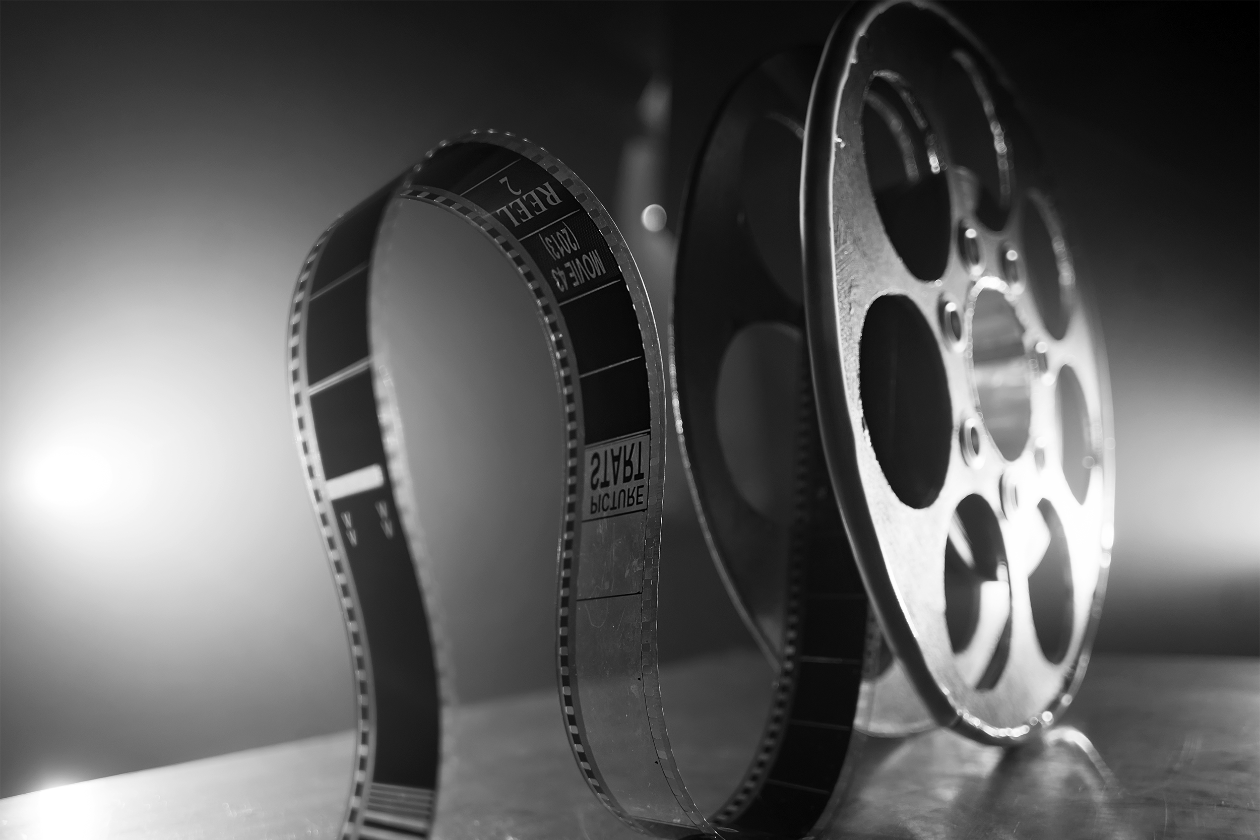Close up of film on a reel of film, black and white on a table, a spotlight on the left background