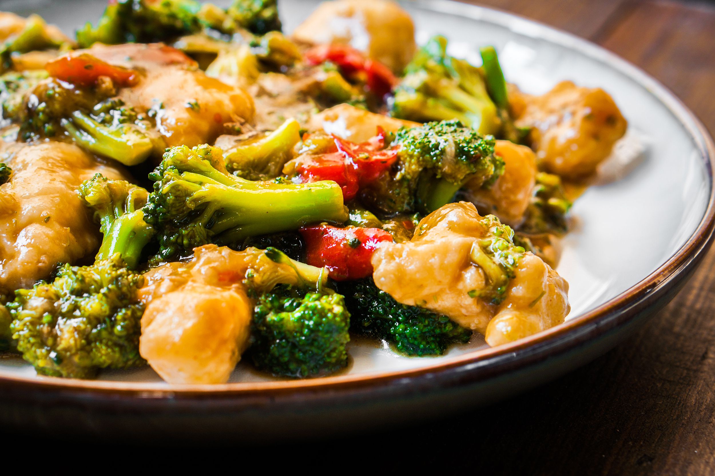 Closeup of quick chicken and broccoli stir fry in a white porcelain bowl with a gold rim, with a blurred background