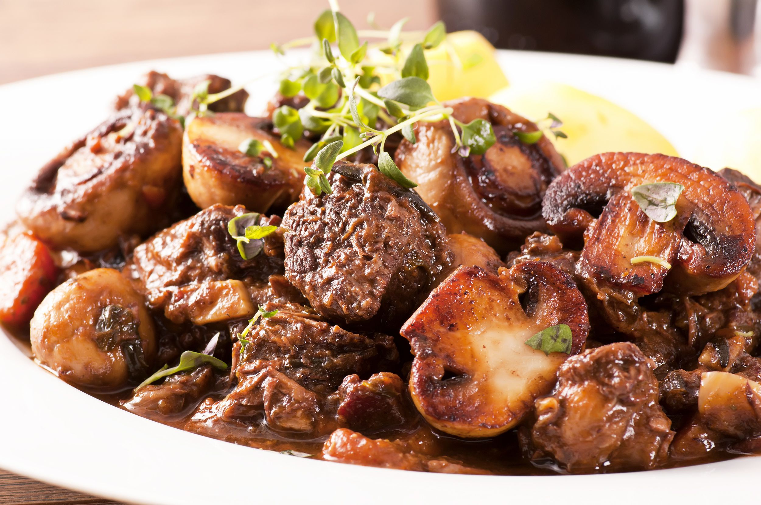 Closeup of beef bourguignon in a wide-rimmed white porcelain bowl with a blurred background