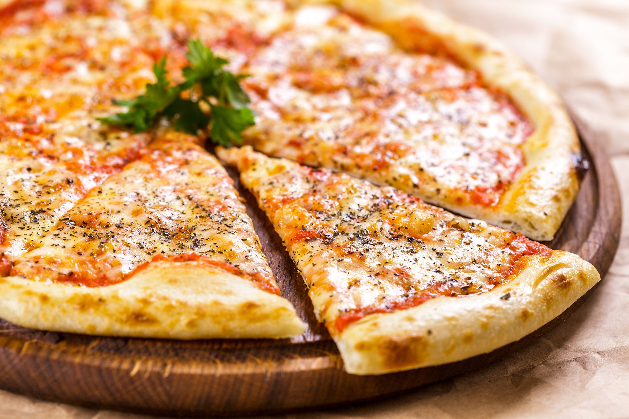 Closeup of cheese pizza with one piece cut and separated on a round wooden serving pizza tray on brown paper, blurred