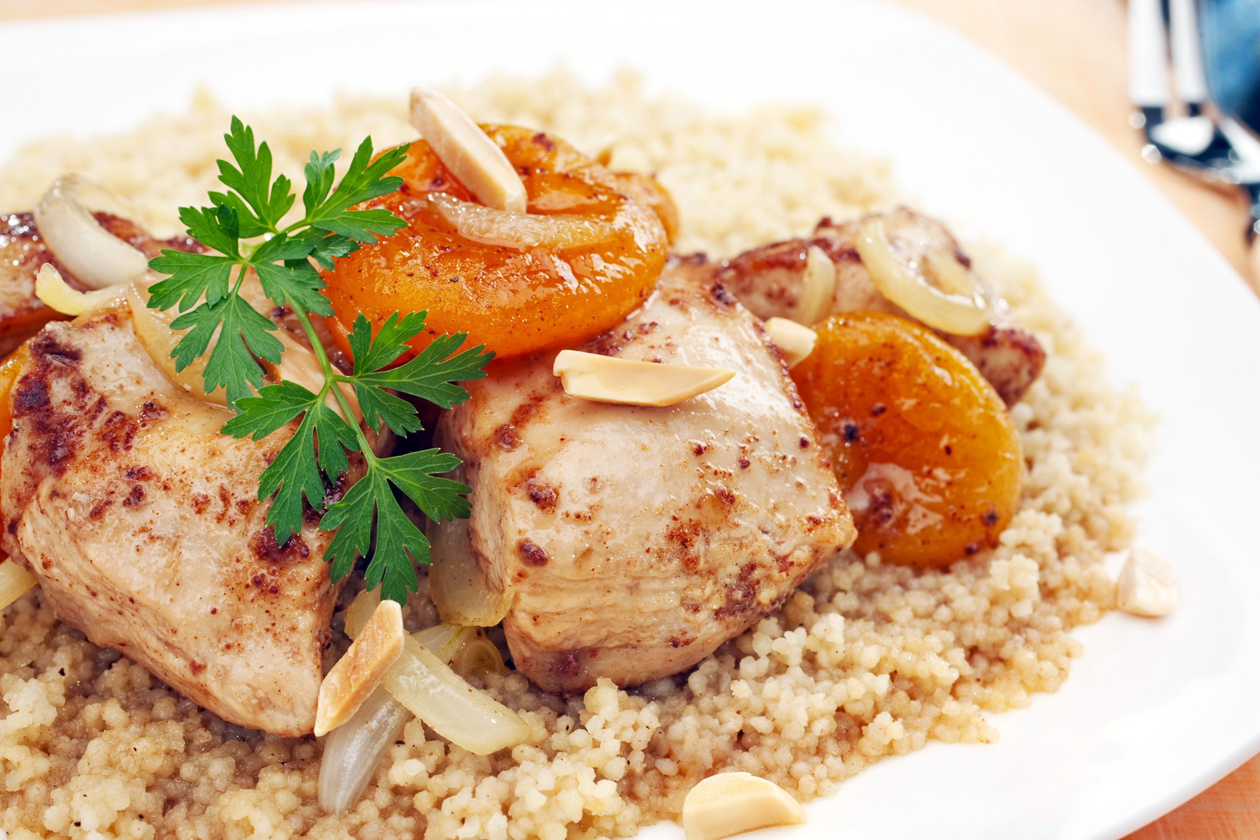 Closeup of chicken tagine with apricots and almonds on a white plate with a blurred background