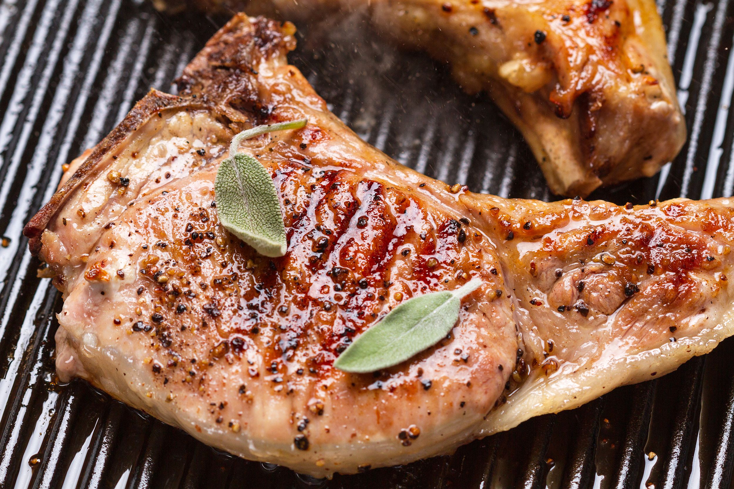 Closeup of one pork chop on a black frying pan grill with another chop in the top right