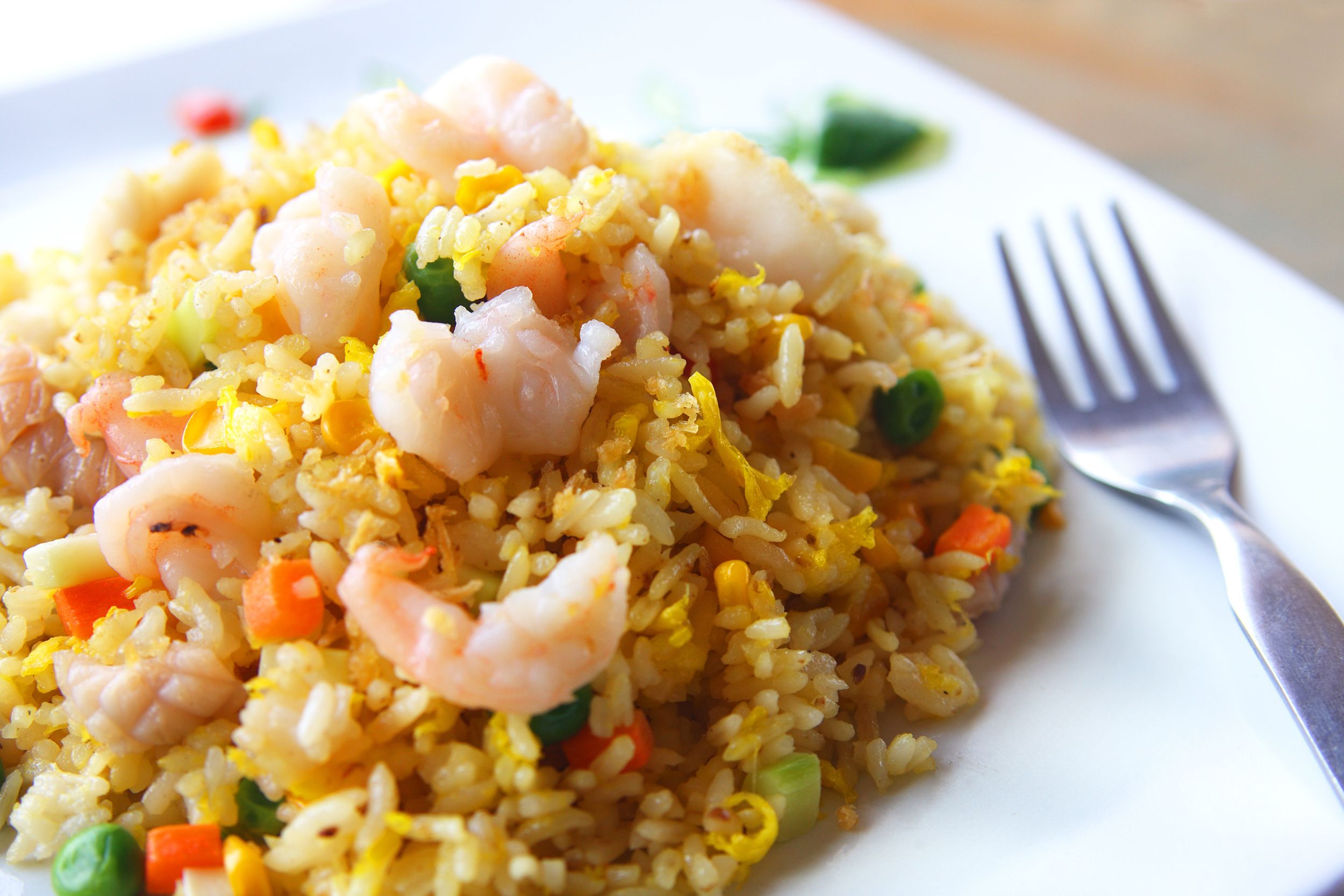 Closeup of shrimp fried rice on a square porcelain white plate, selective focus, with a fork on the plate to the right, with a blurred background