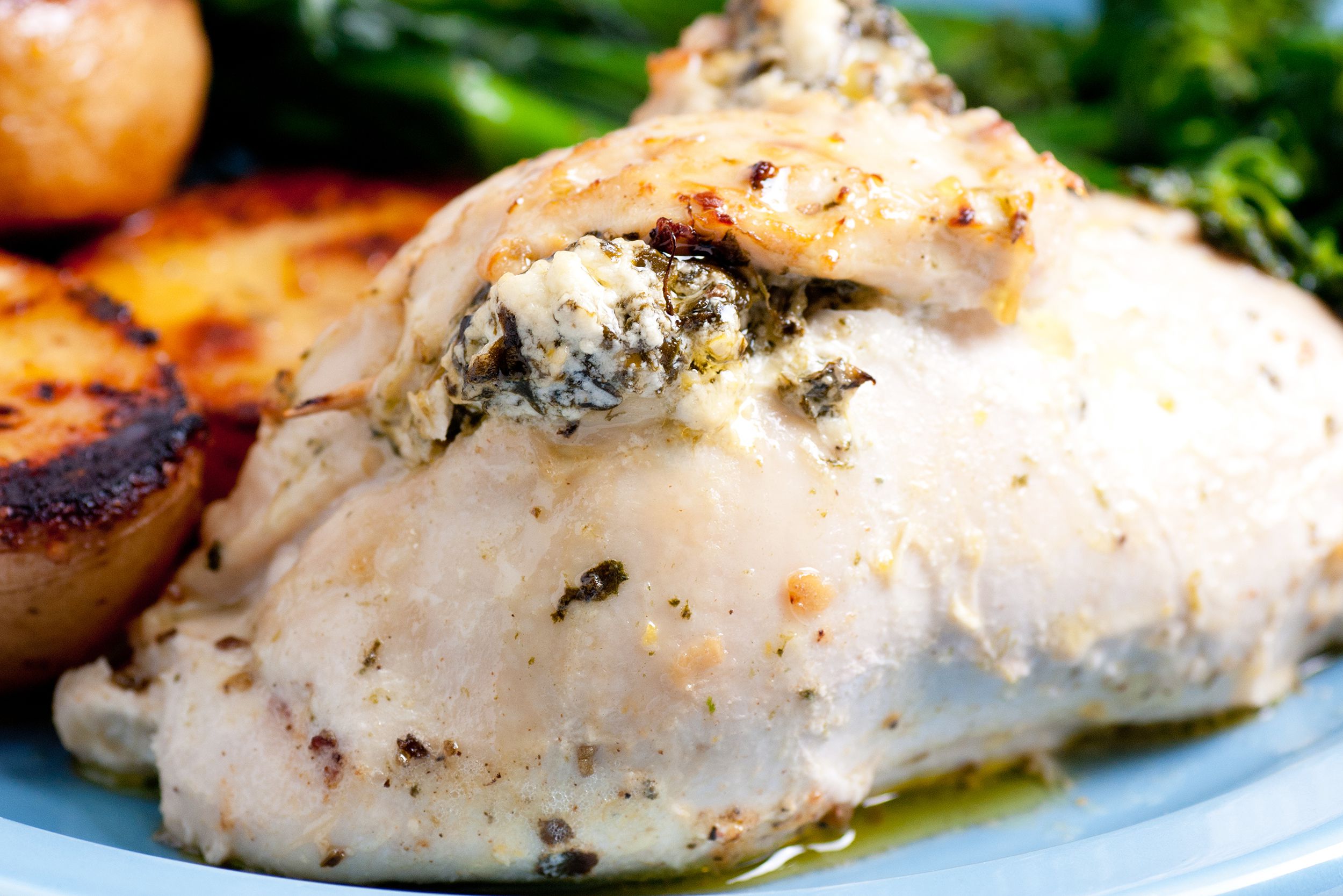 Closeup of spinach and feta stuffed chicken breast surrounded by spinach and sweet potatoes on a light blue plate