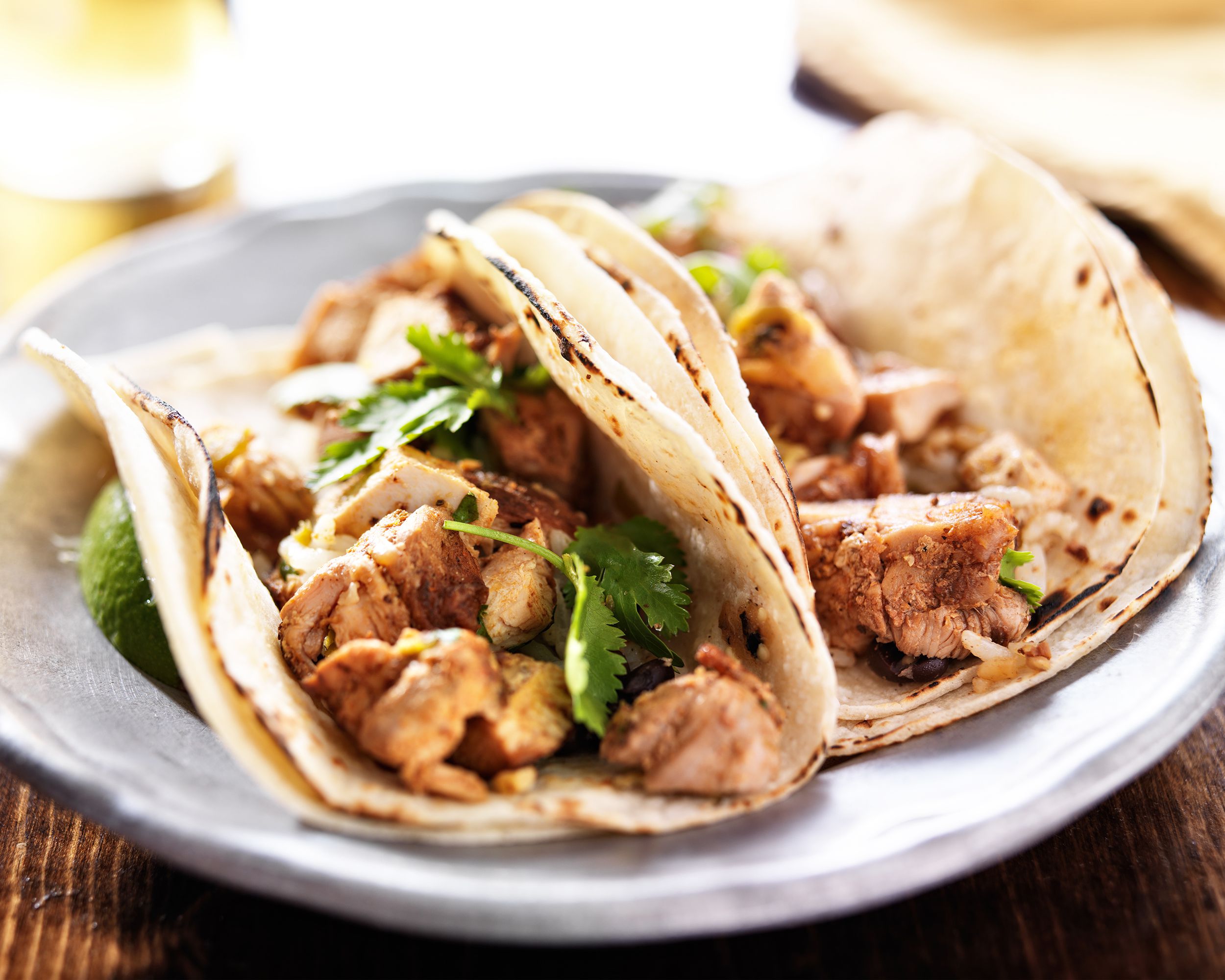 Closeup of two easy weeknight chicken tacos on a periwinkle ceramic plate with a blurred background of a table and utensils