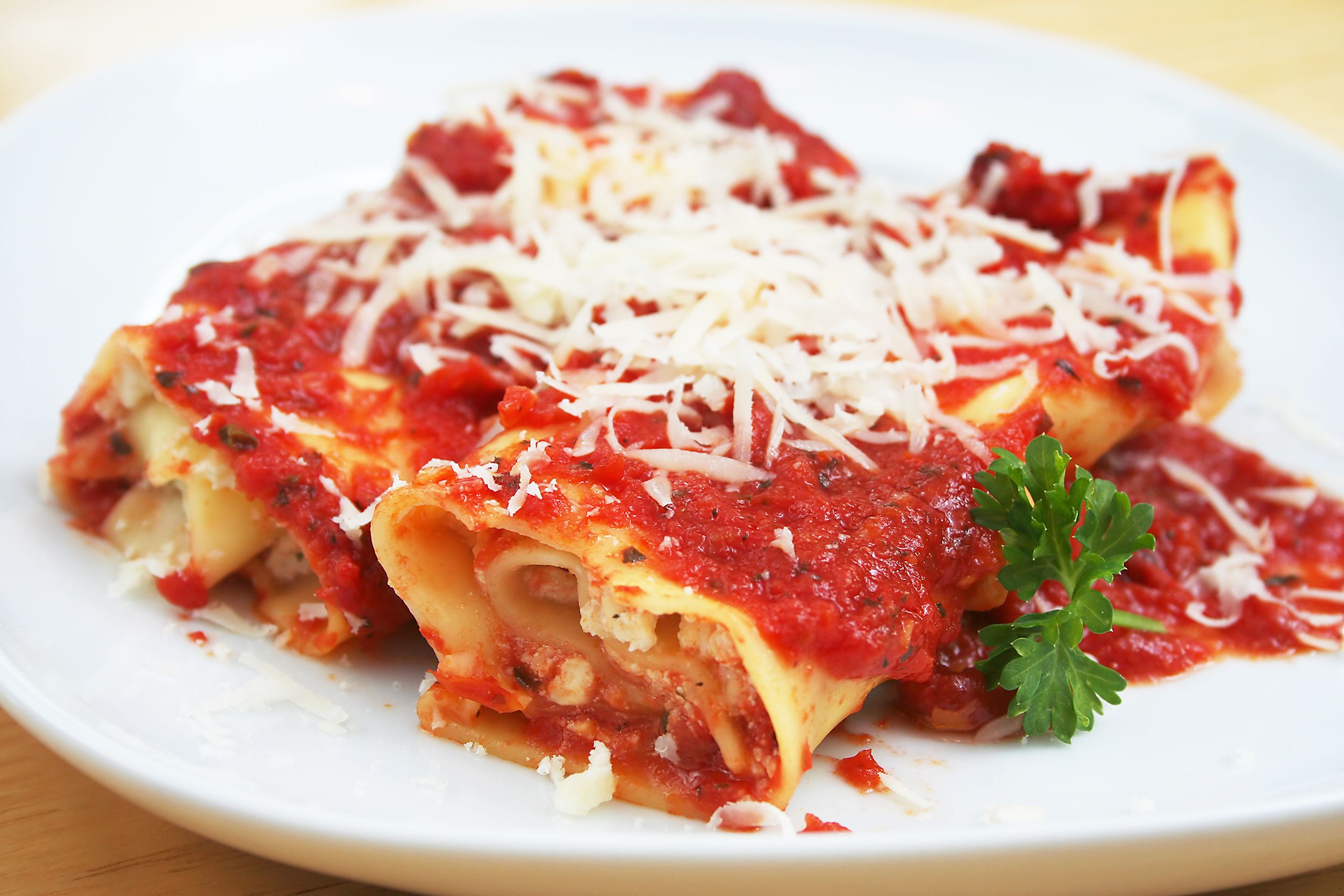 Closeup of a piece of cheese stuffed manicotti on a white porcelain plate with the table shown in the corners of the image