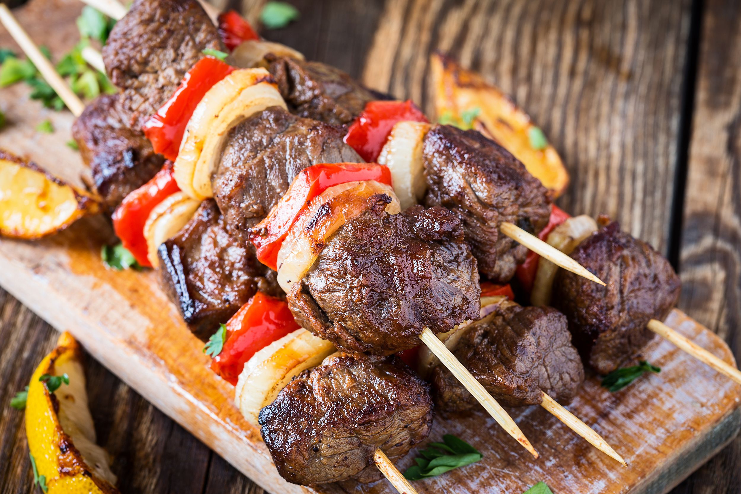 Closeup of a pile of five the best shish kebab skewers on a narrow wooden serving board, selective focus, on a rustic wooden table blurred in the background