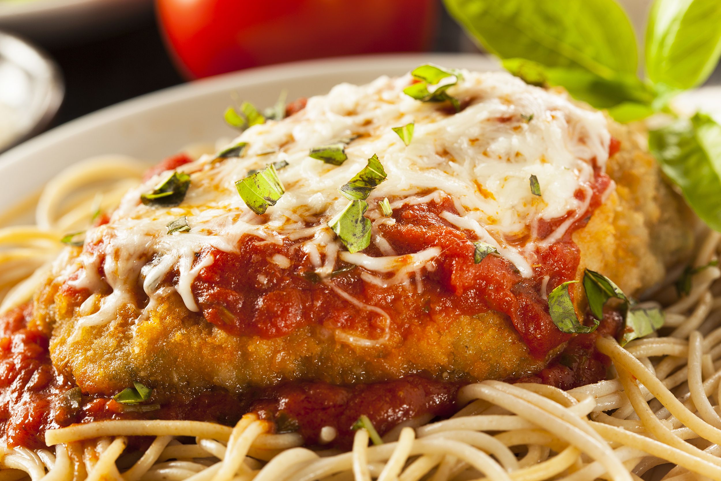 Easy chicken parmesan on spaghetti noodles on a white plate with a blurred background of ingredients