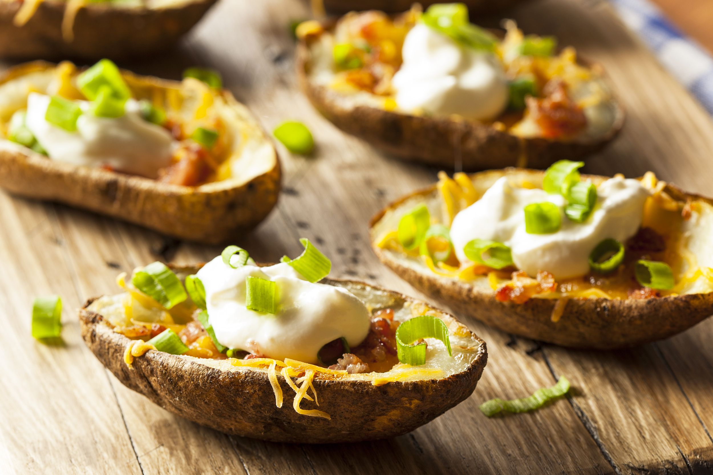 Five loaded baked potatoes on a wooden serving plate with a blurred background