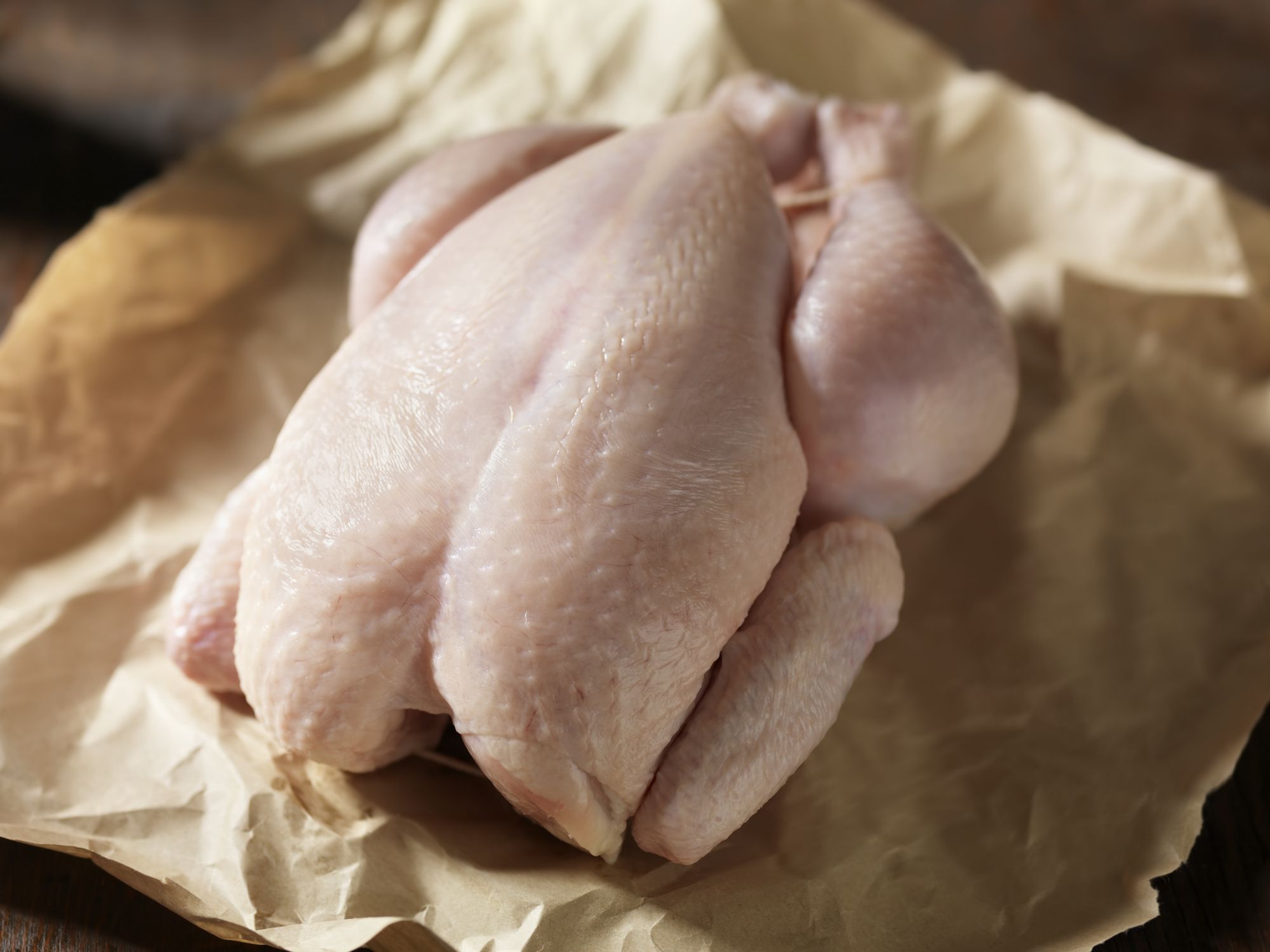 Focus on a raw whole chicken on butchers paper with a blurred background