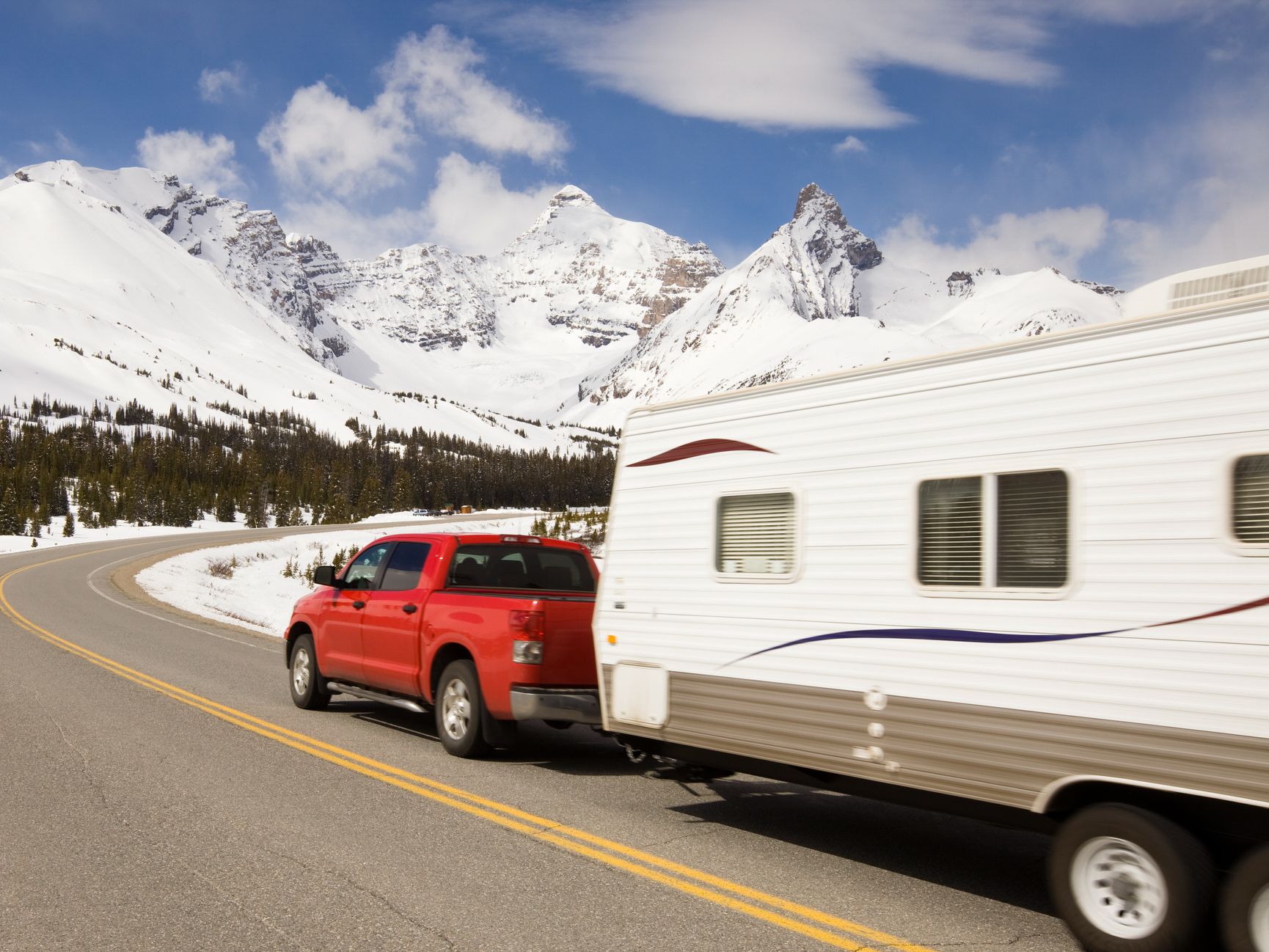 Pickup truck and travel trailer passing by on a highway in the mountains.