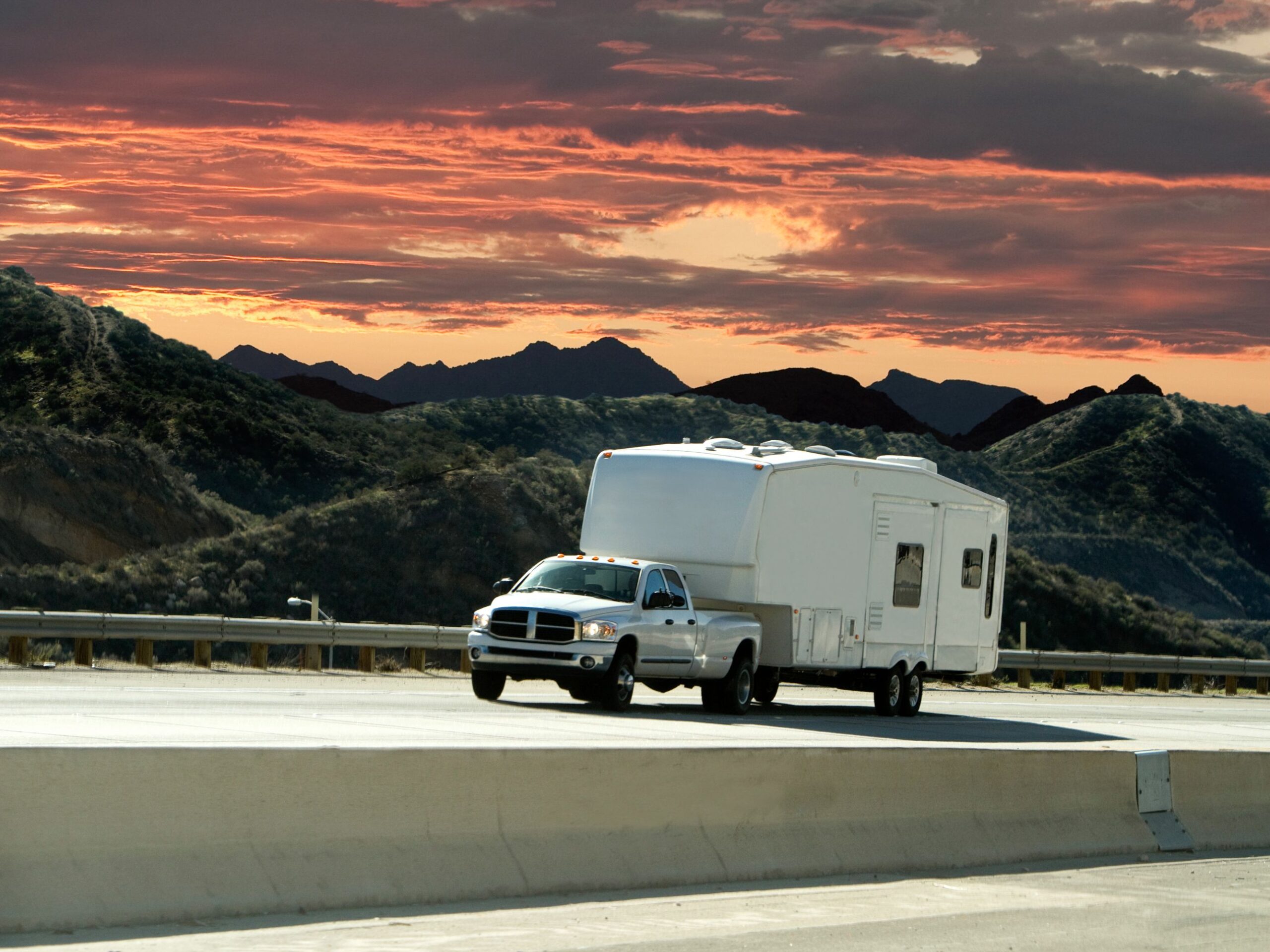A truck pulling a trailer with a beautiful sunset in the background.