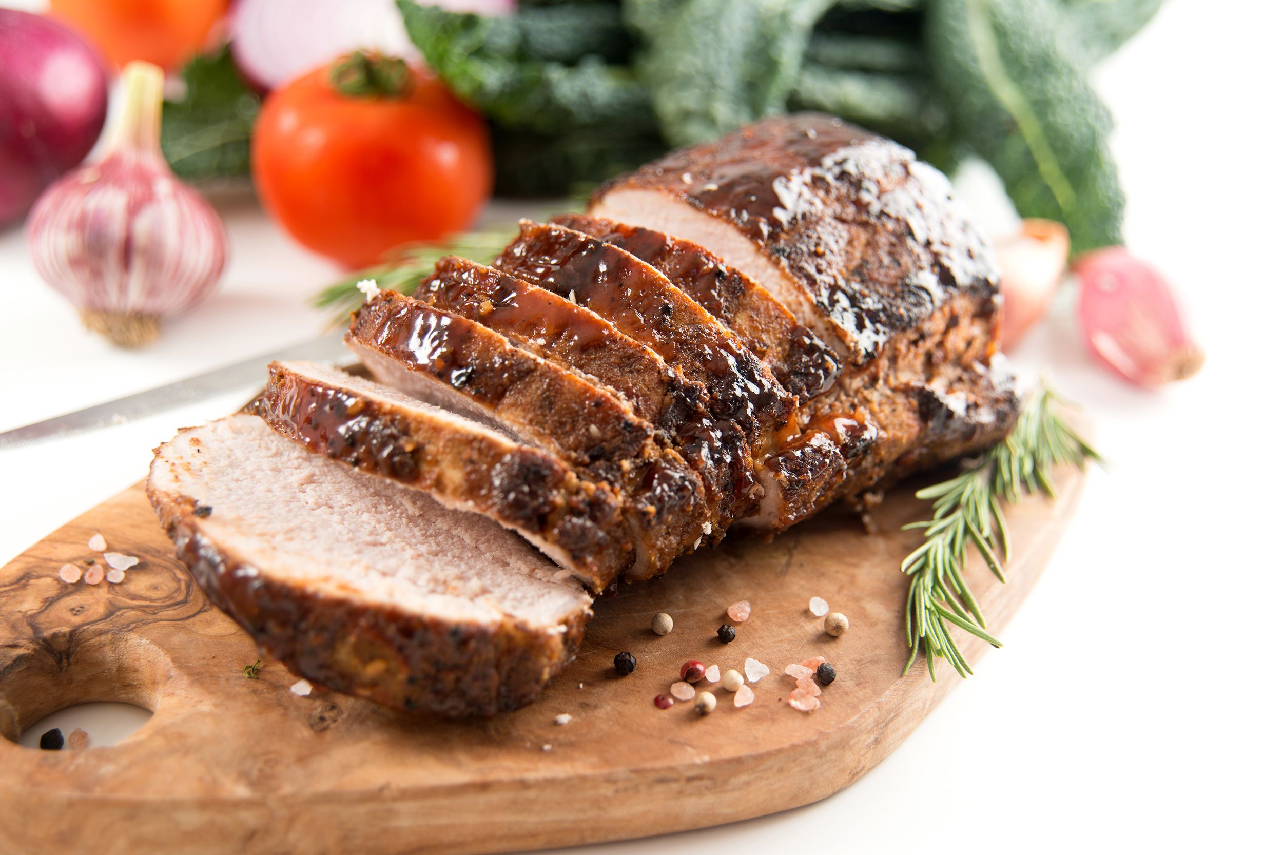 Roast pork loin with rosemary and garlic on an artisanal serving board, selective focus, on a white table with ingredients blurred in the background