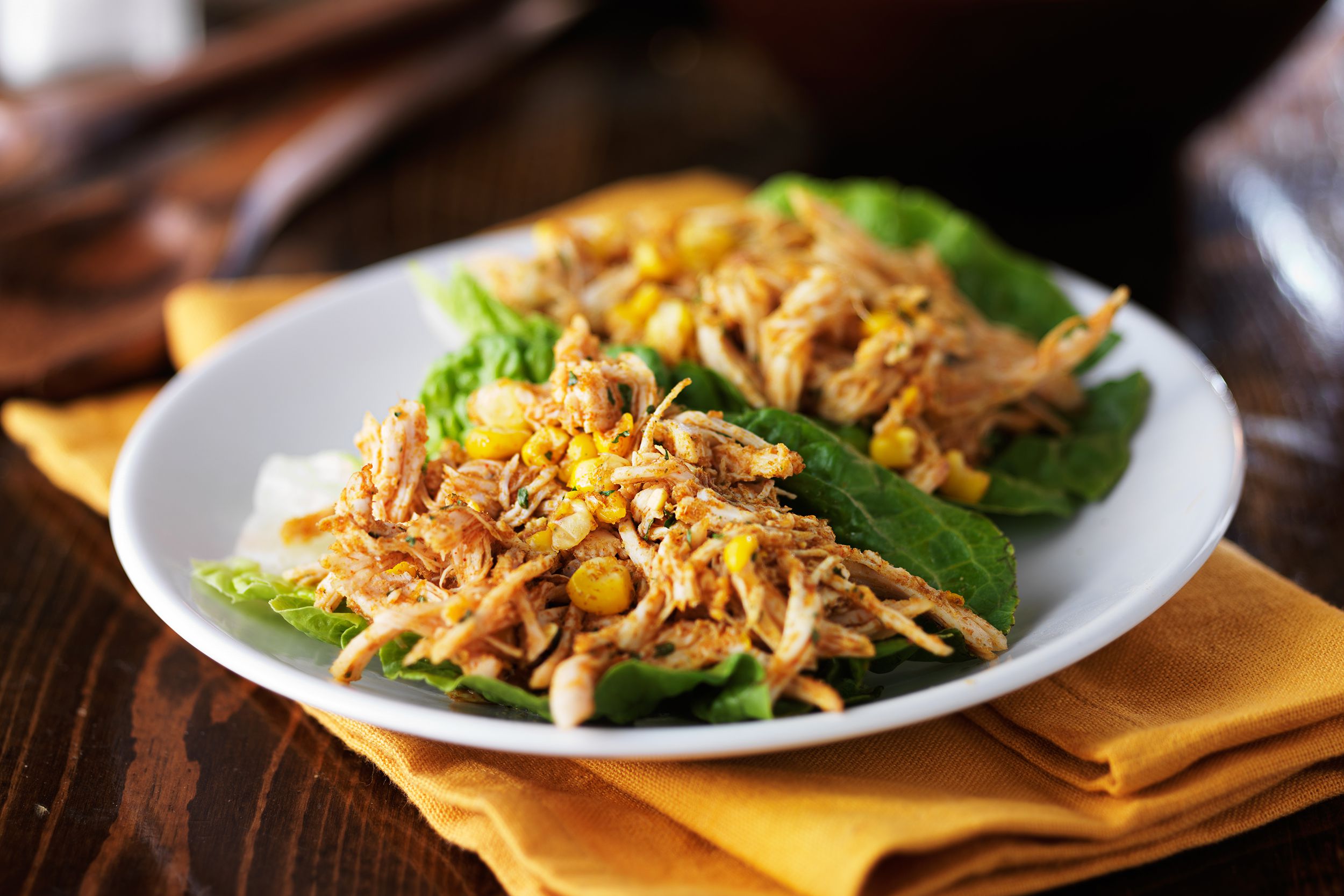 Selective focus of easy shredded chicken in the slow cooker on a white plate and a yellow ochre napkin on a wooden table