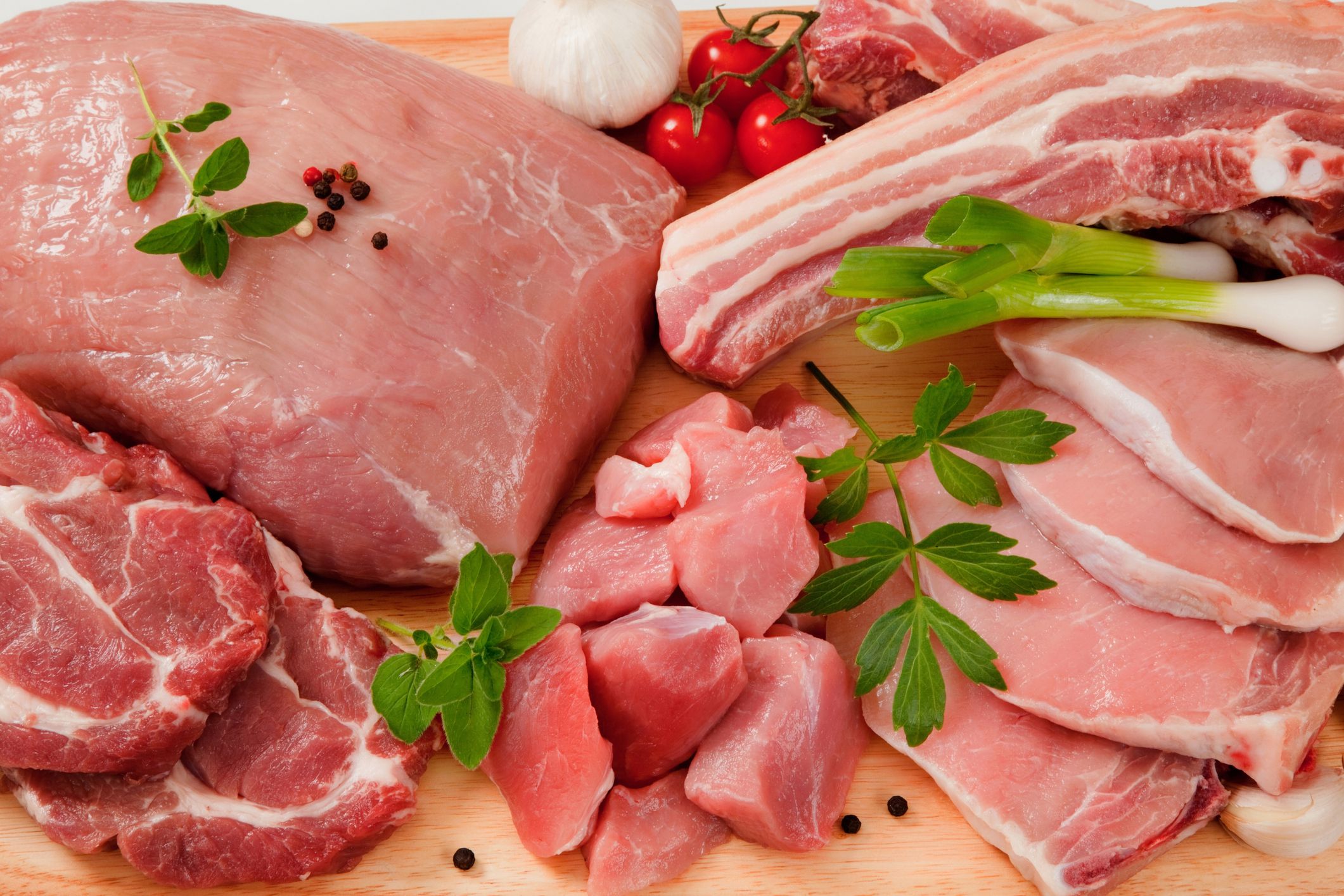 Several different kinds of raw cuts of pork meat on a wooden cutting board