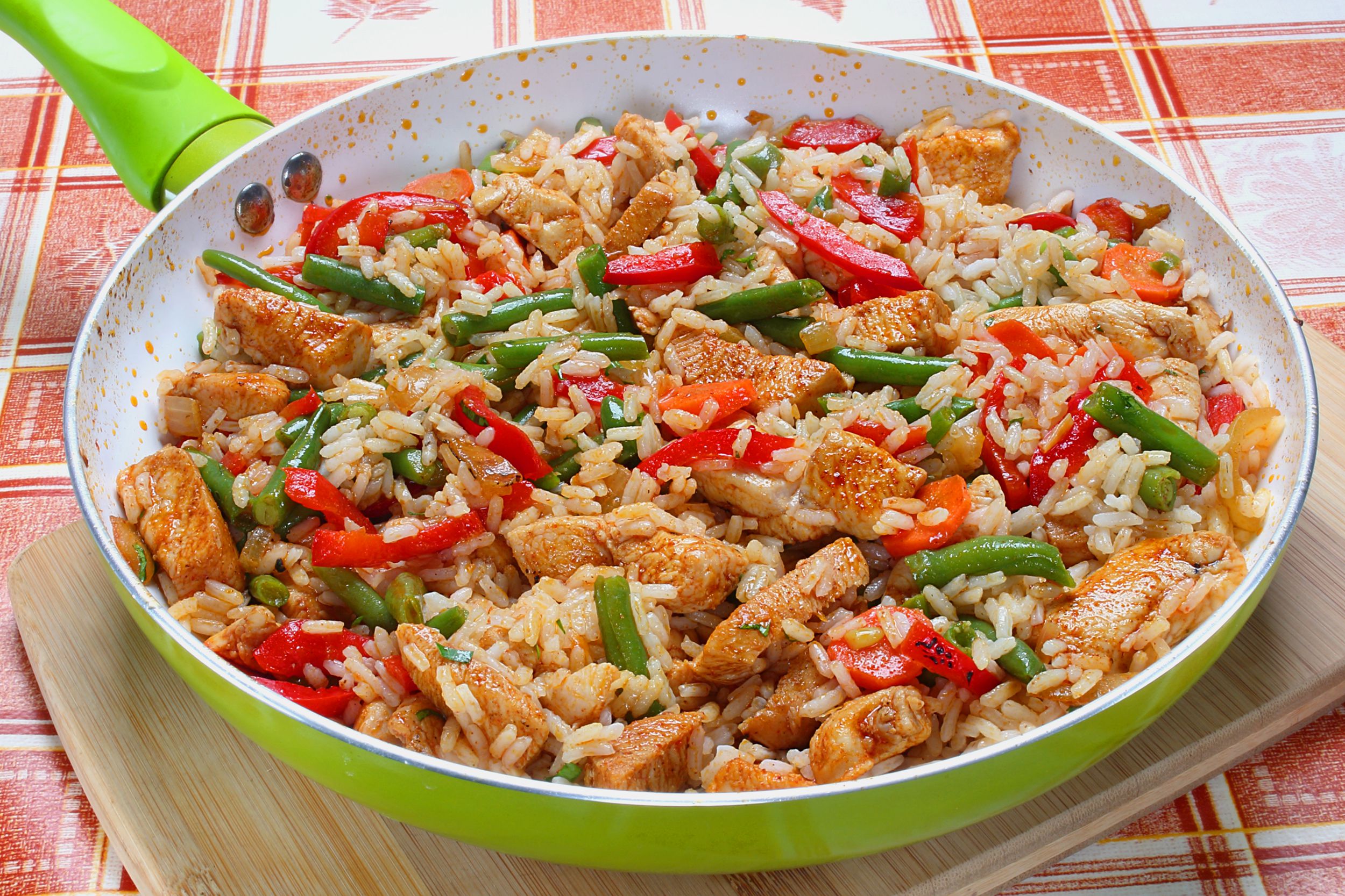 The best chicken and rice in a lime green skillet on a bamboo cutting board on a red and white plaid tablecloth