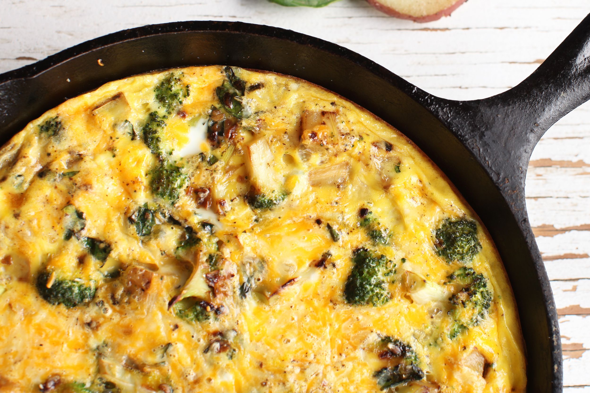 Top view of broccoli and cheddar frittata in a cast iron skillet on a white wooden table